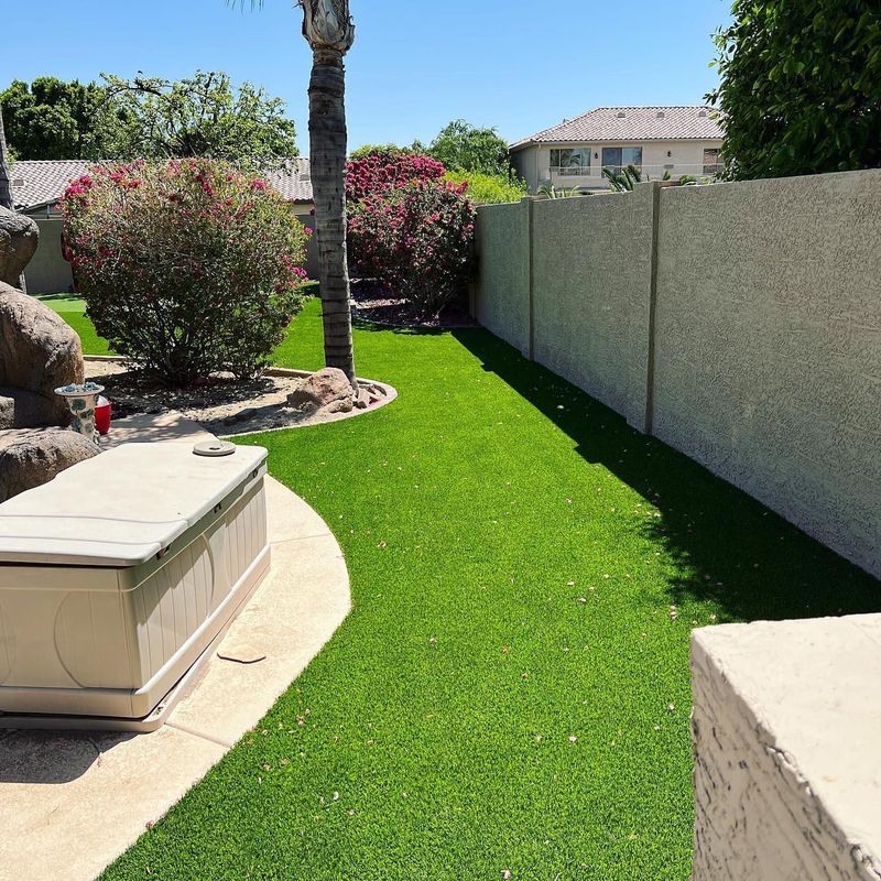 Lush artificial turf side yard with flowering shrubs along a stucco wall