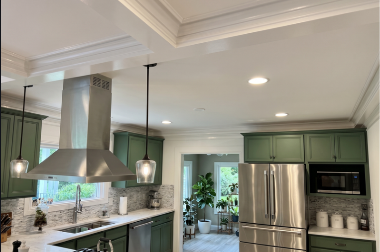 Kitchen with a recessed coffered ceiling, green cabinets, stainless steel range hood, and crown molding