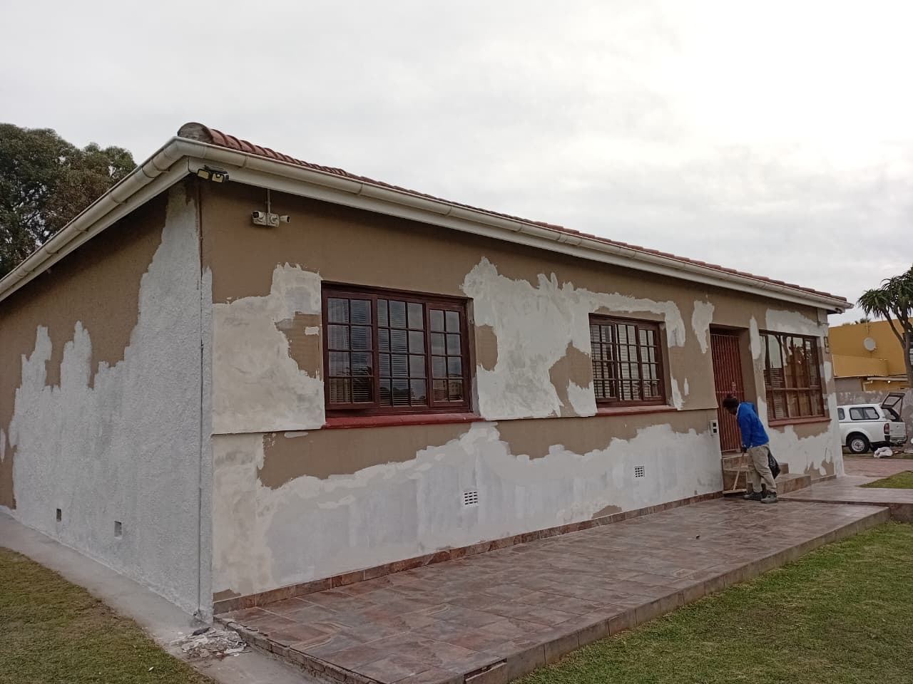 Before: House exterior with peeling paint and exposed plaster patches, brown walls needing renovation