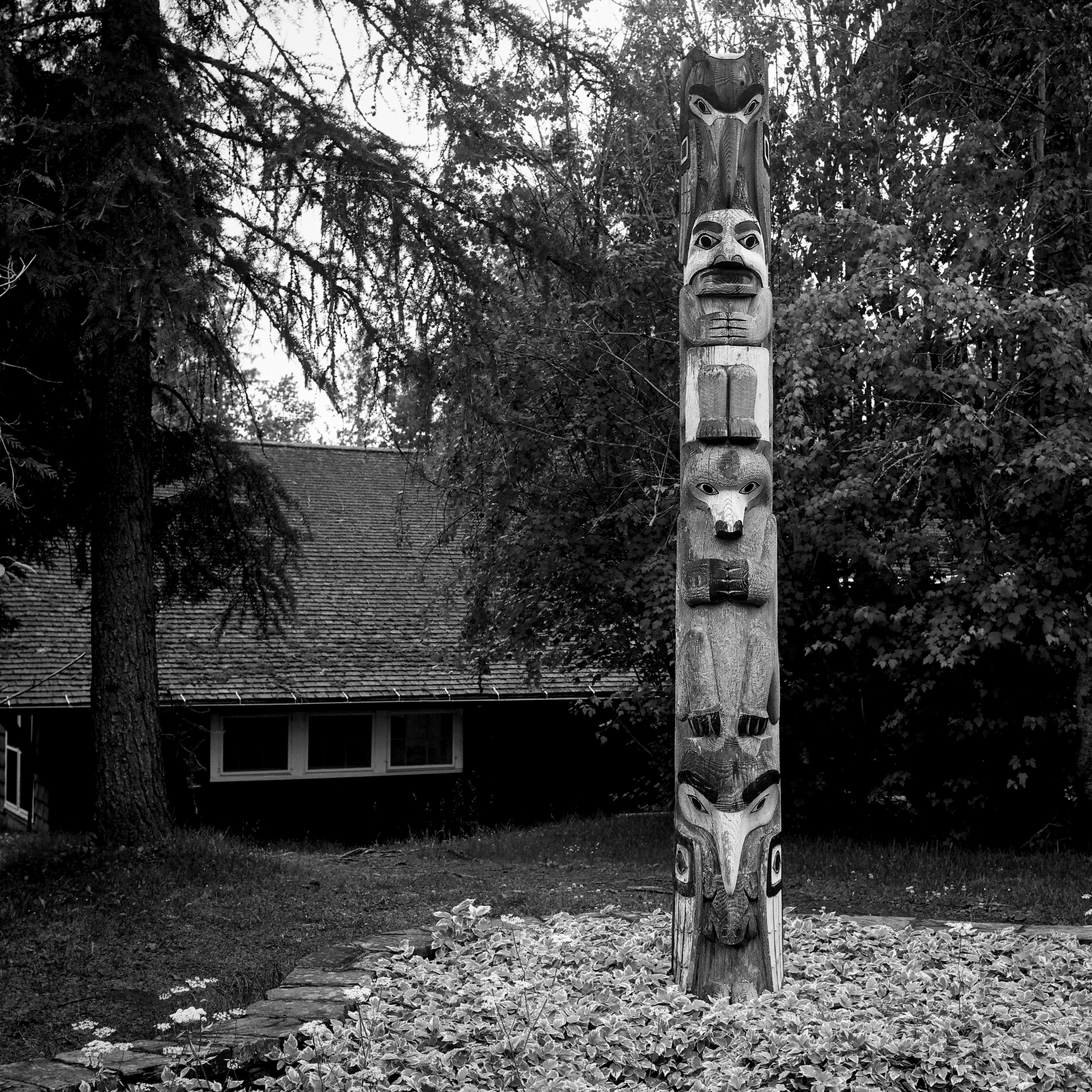 Native American totem pole with carved animal faces standing before rustic wooden lodge in forest