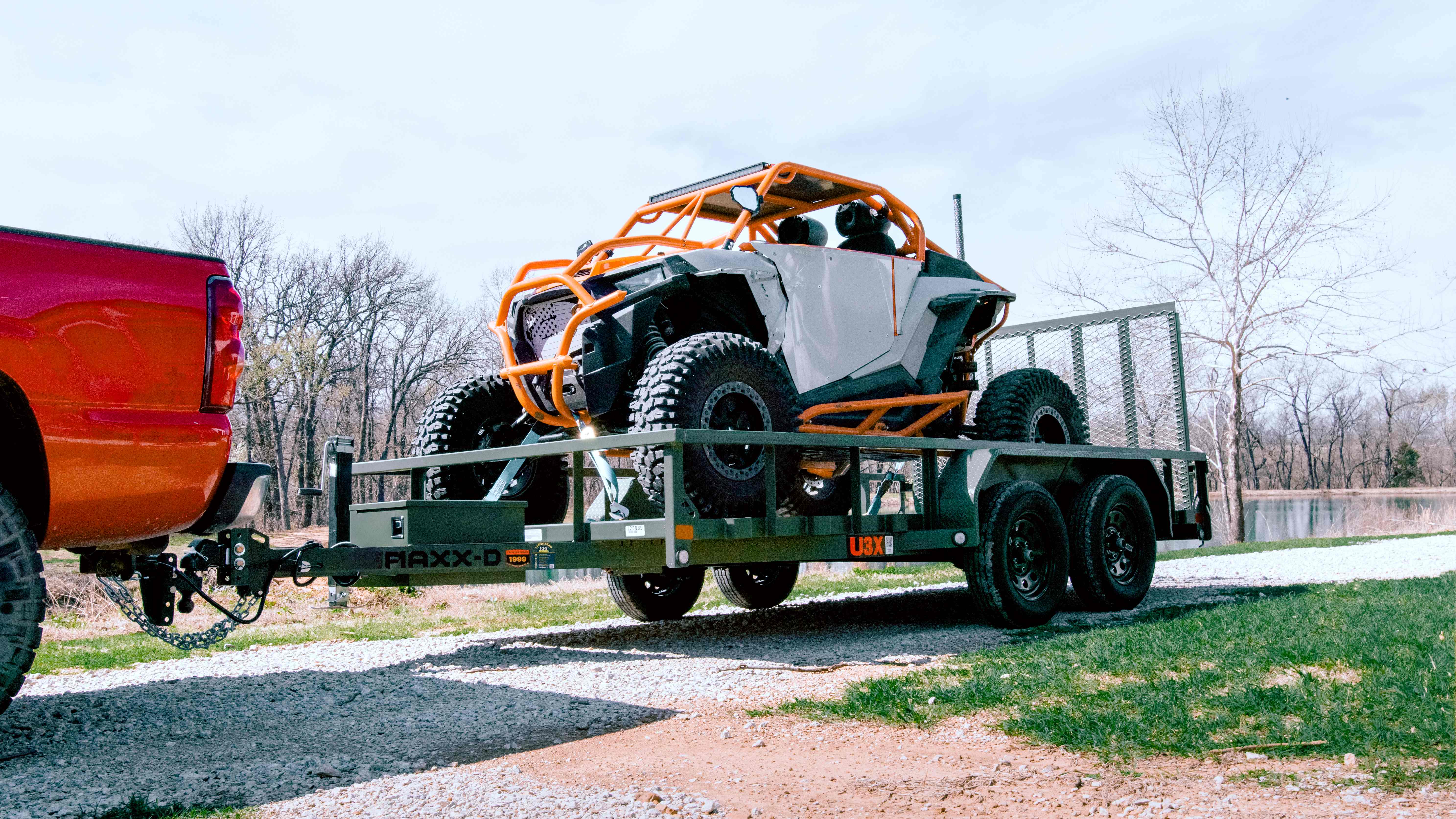 Orange UTV loaded on the Maxx-D UX3 utility trailer hitched to a red truck