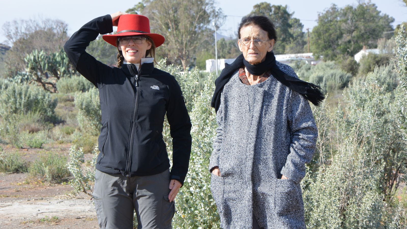 Two artists posing outdoors with dryland vegetation