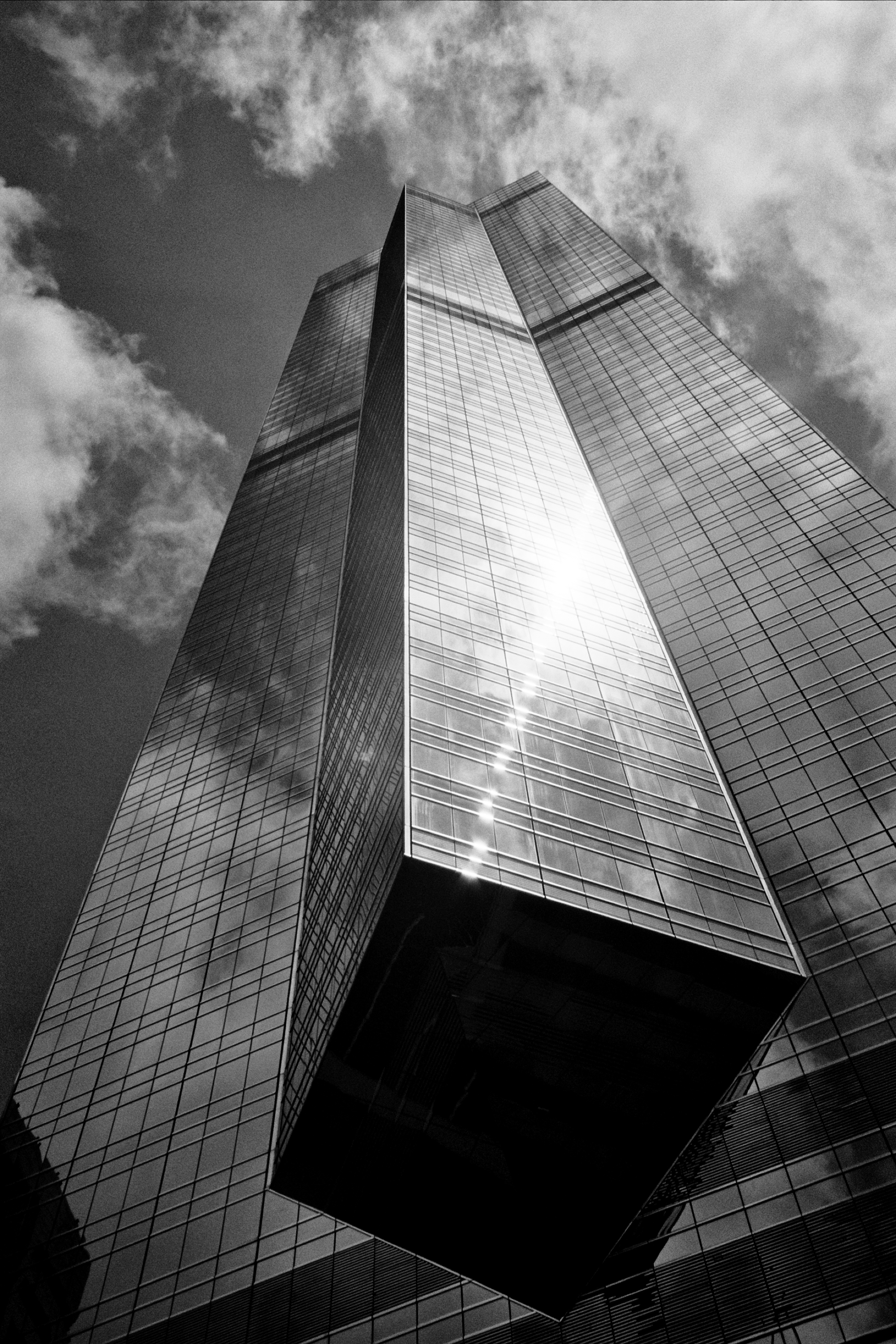 Modern glass skyscraper shot from below with dramatic clouds and sun reflection