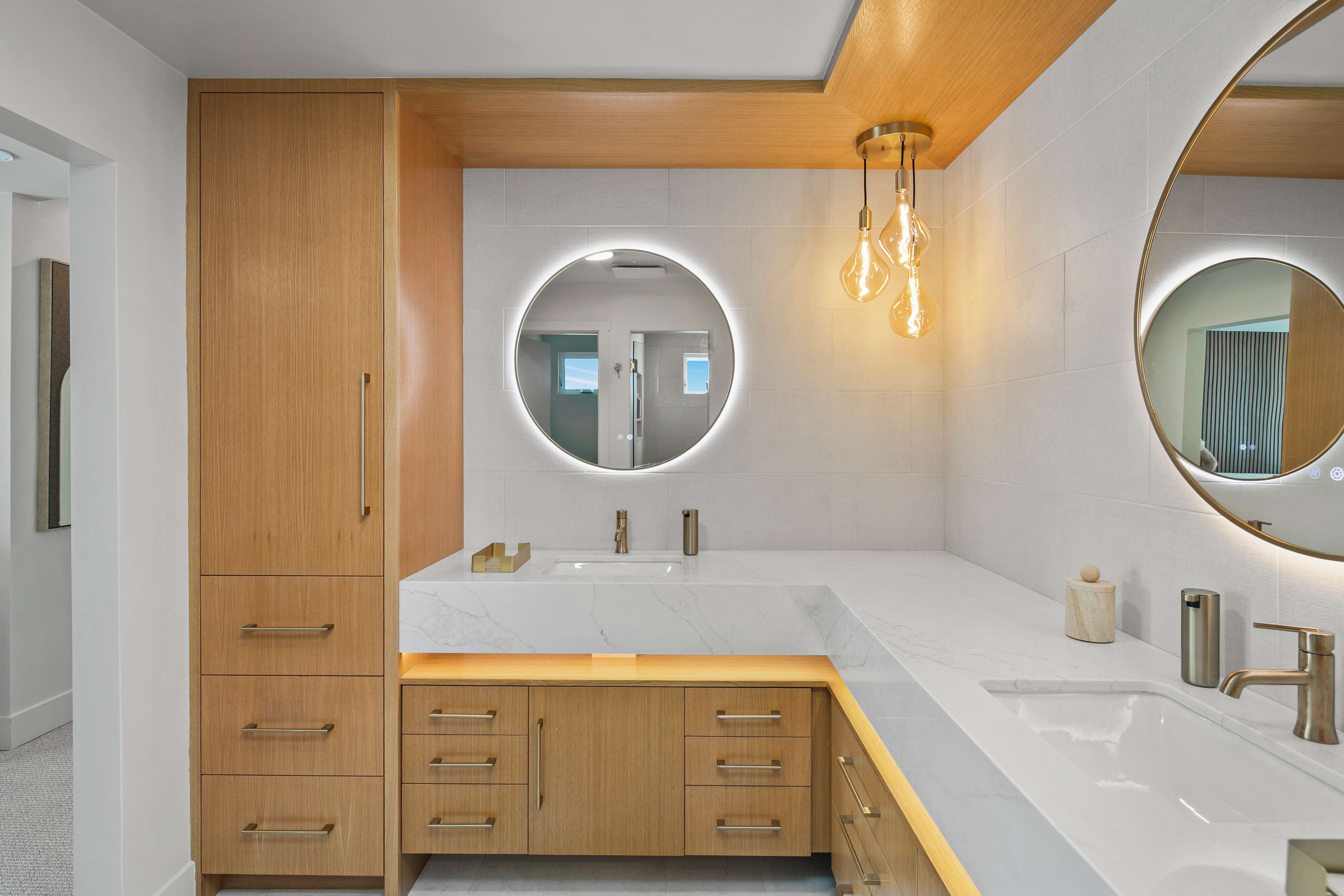 Dual-vanity bathroom with illuminated round mirrors and oak cabinetry