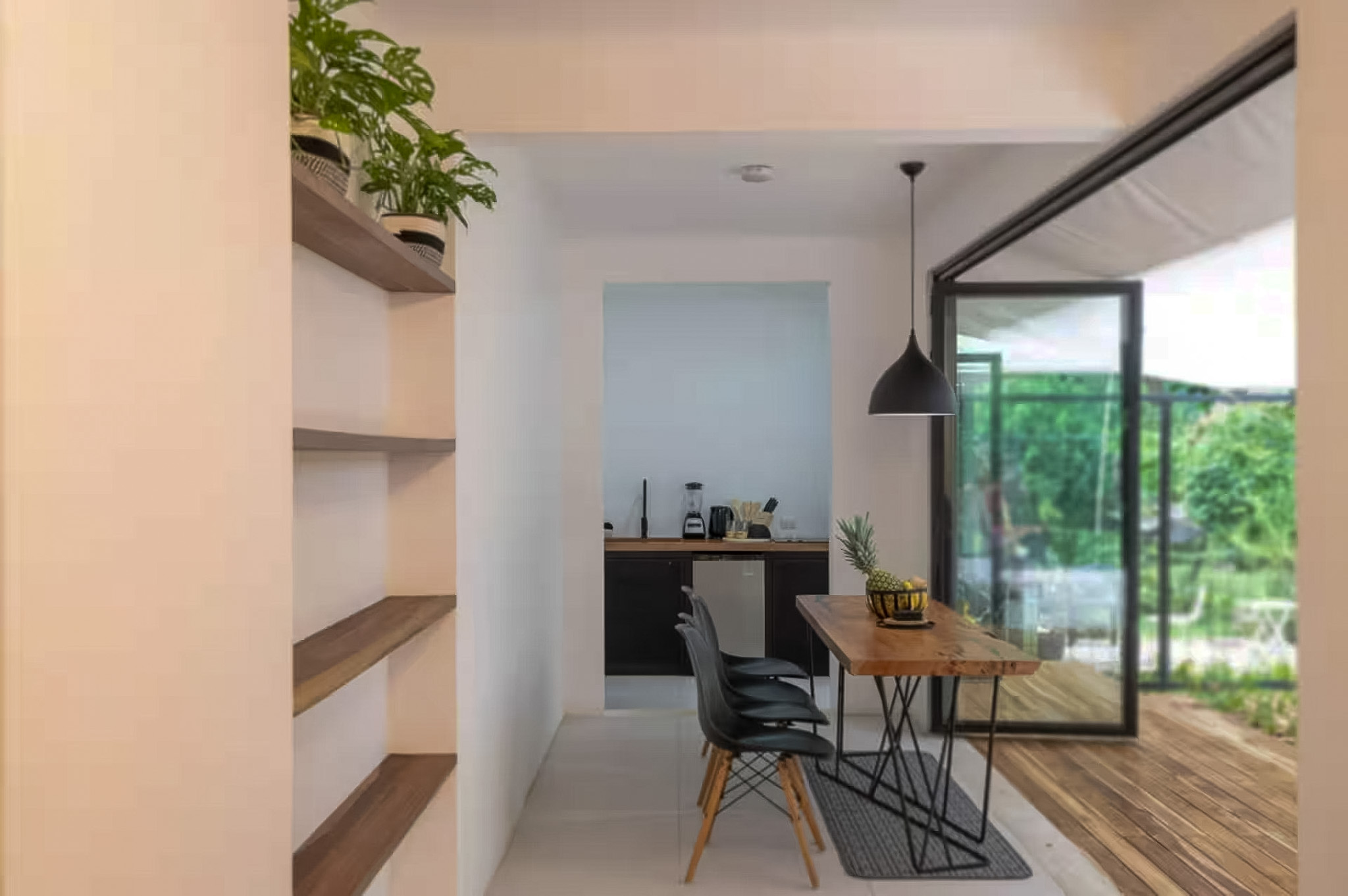 Modern living space with open shelving, dining table, kitchen, and garden views through glass doors