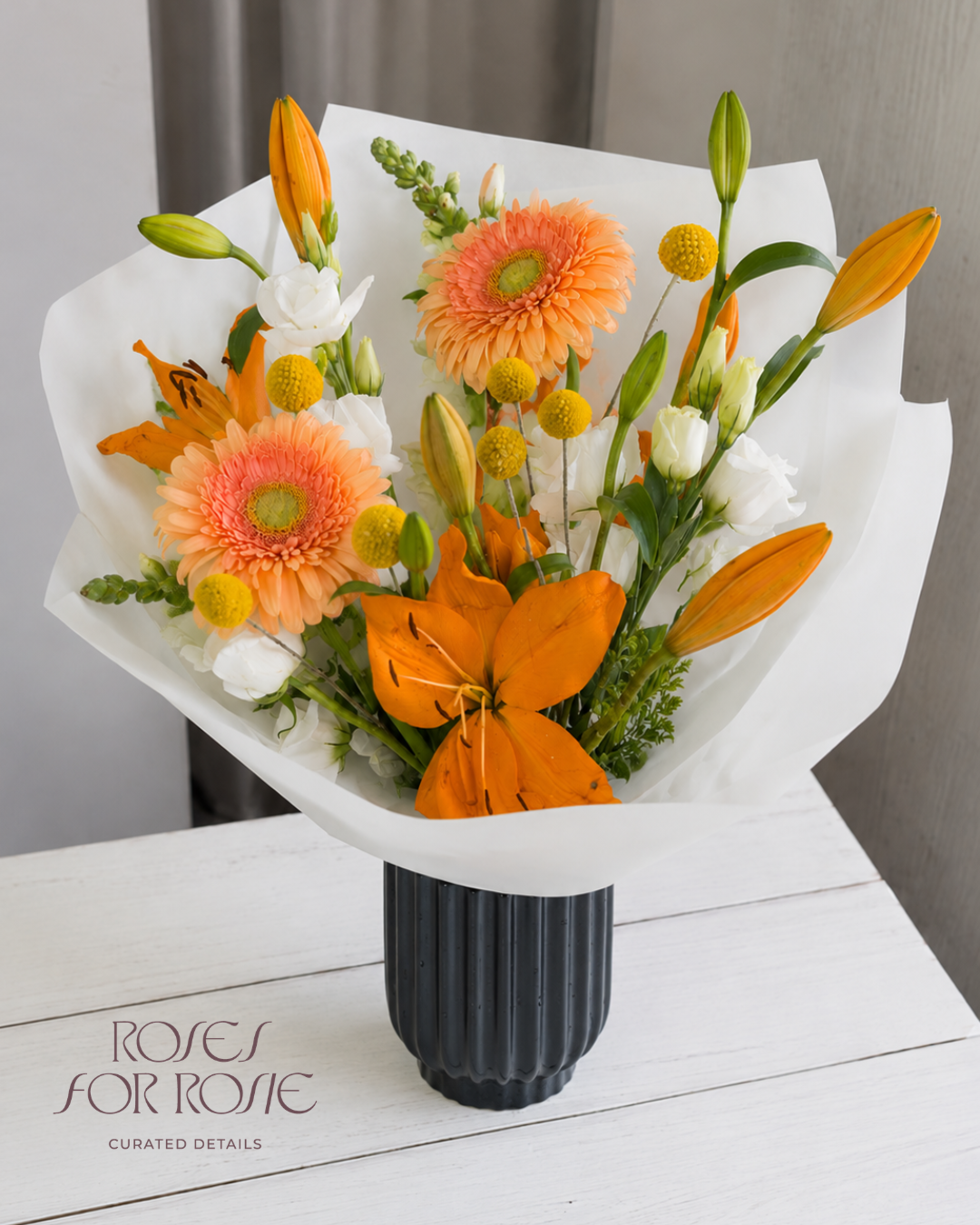 Ramo naranja con gerberas y lilies en florero negro - Roses for Rosie
