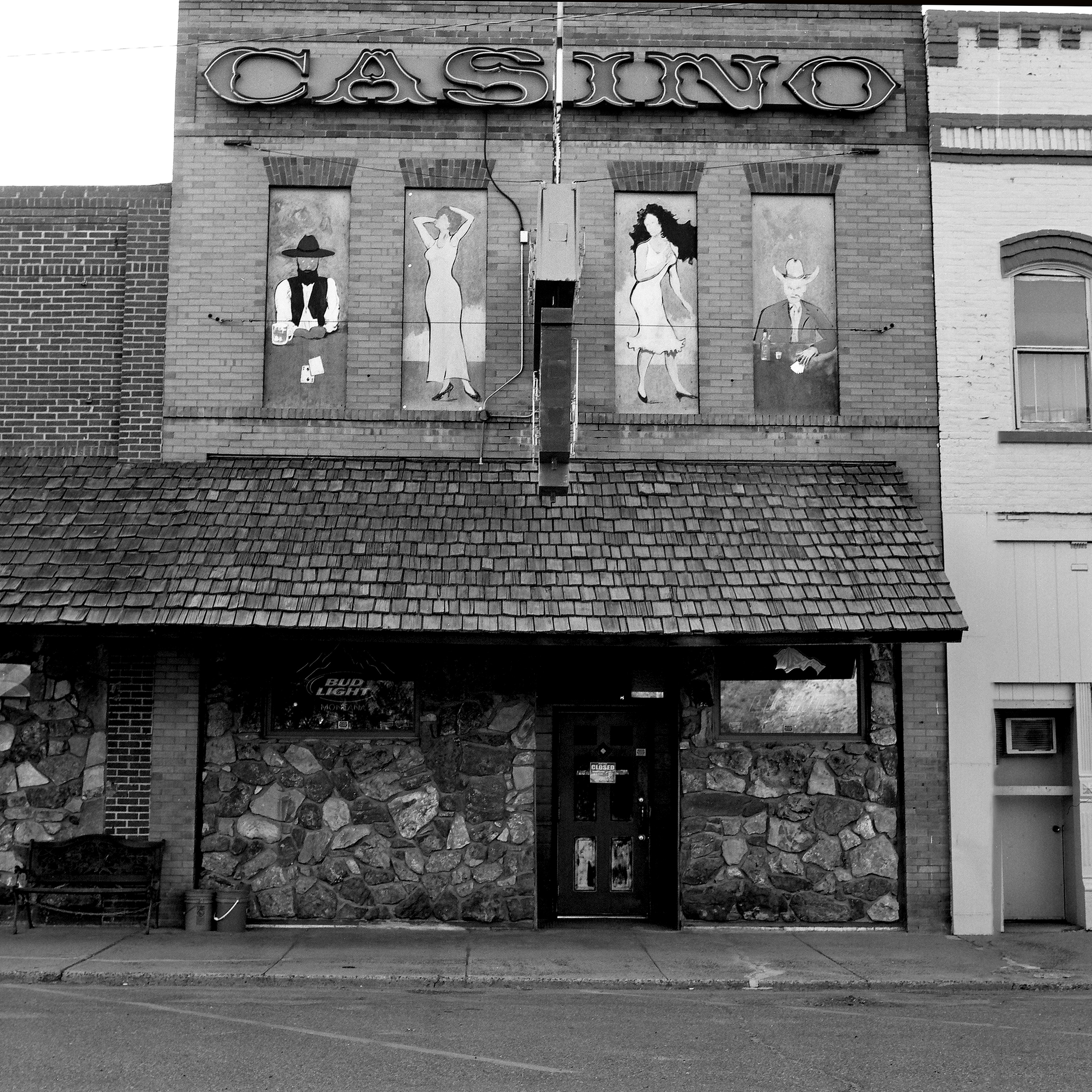 Old casino building with painted murals of cowboys and showgirls on brick facade with wood shingle awning