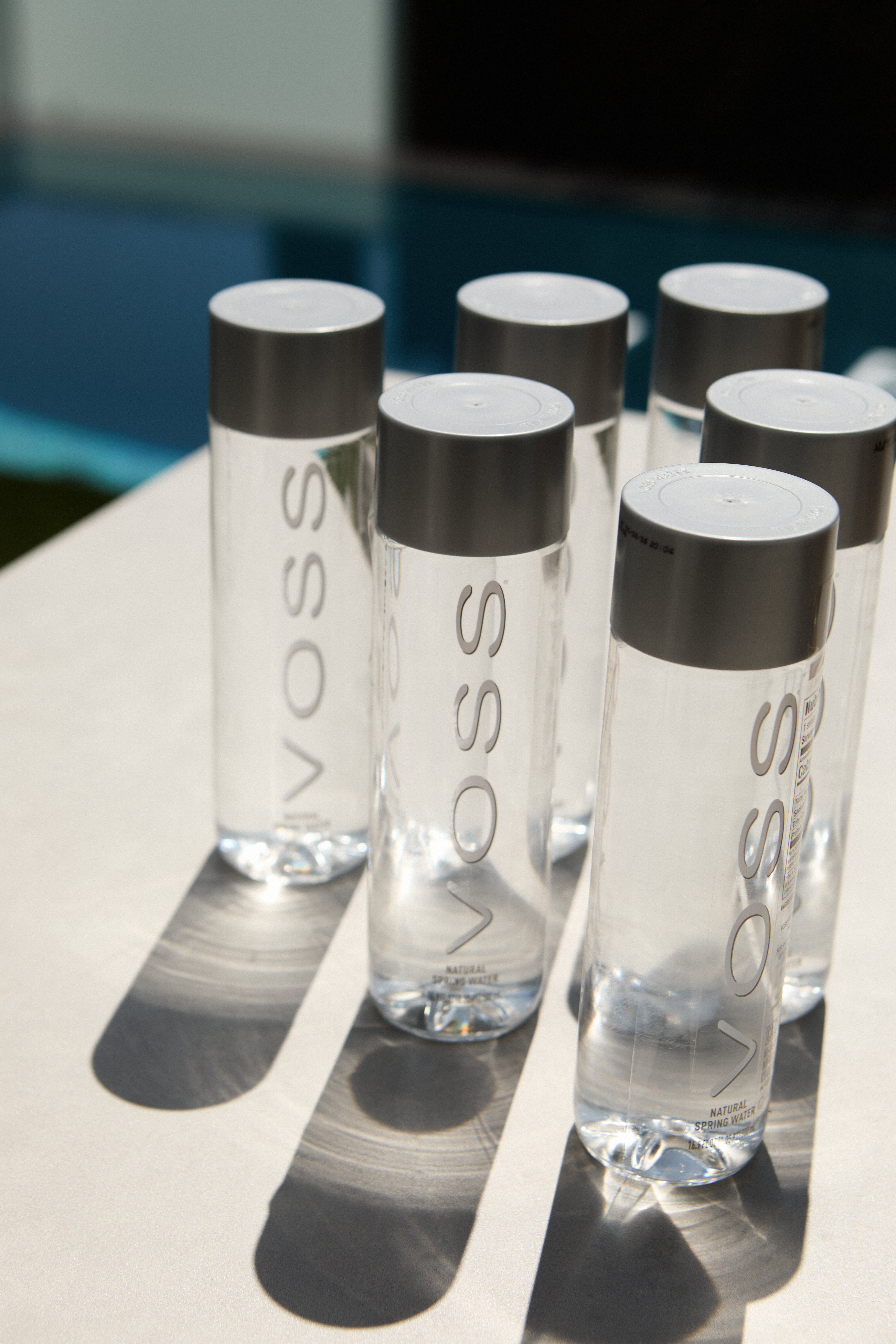 Six VOSS spring water bottles arranged on a white table in sunlight
