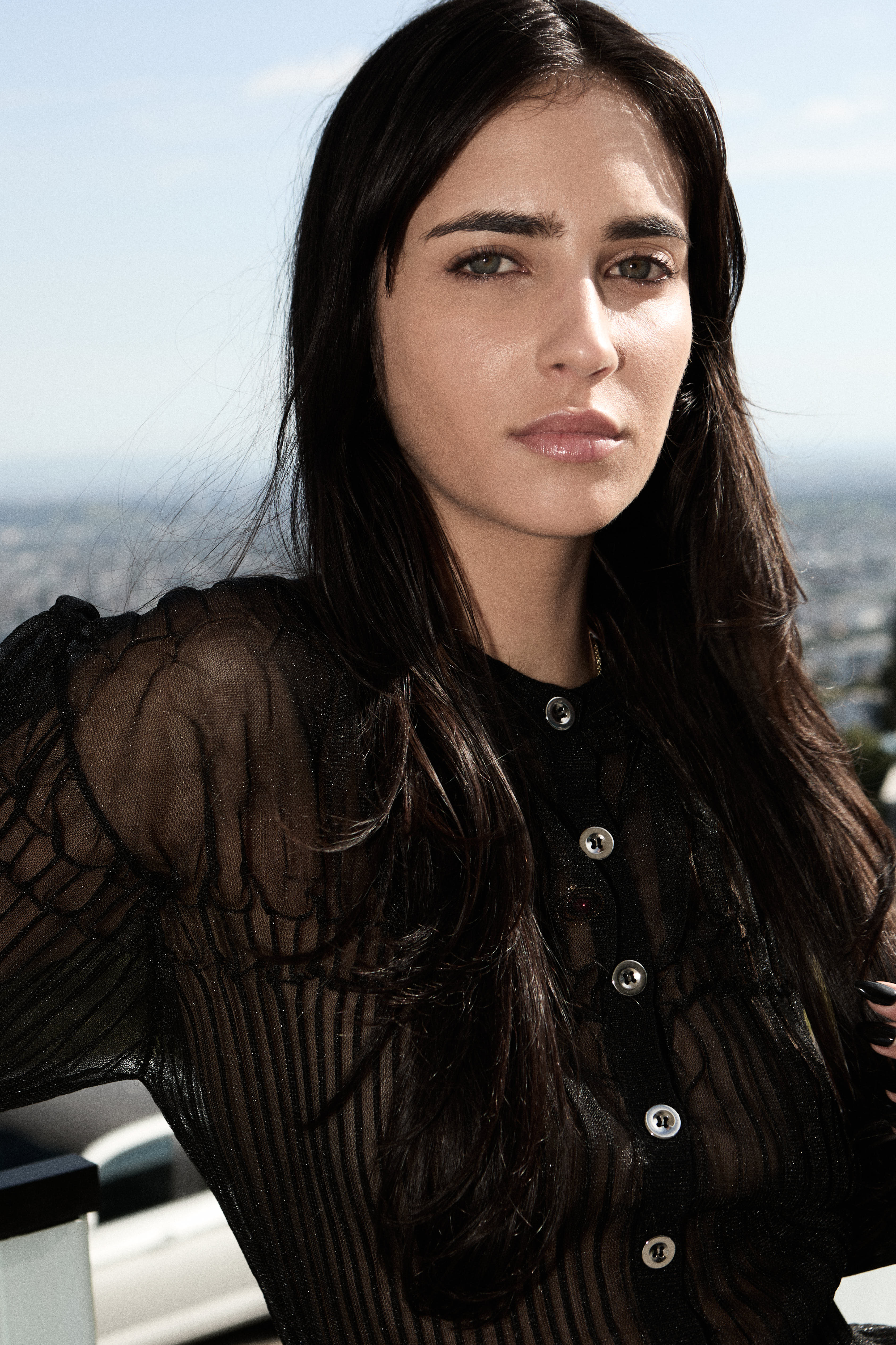 Close-up portrait of a brunette in a sheer black top on a rooftop