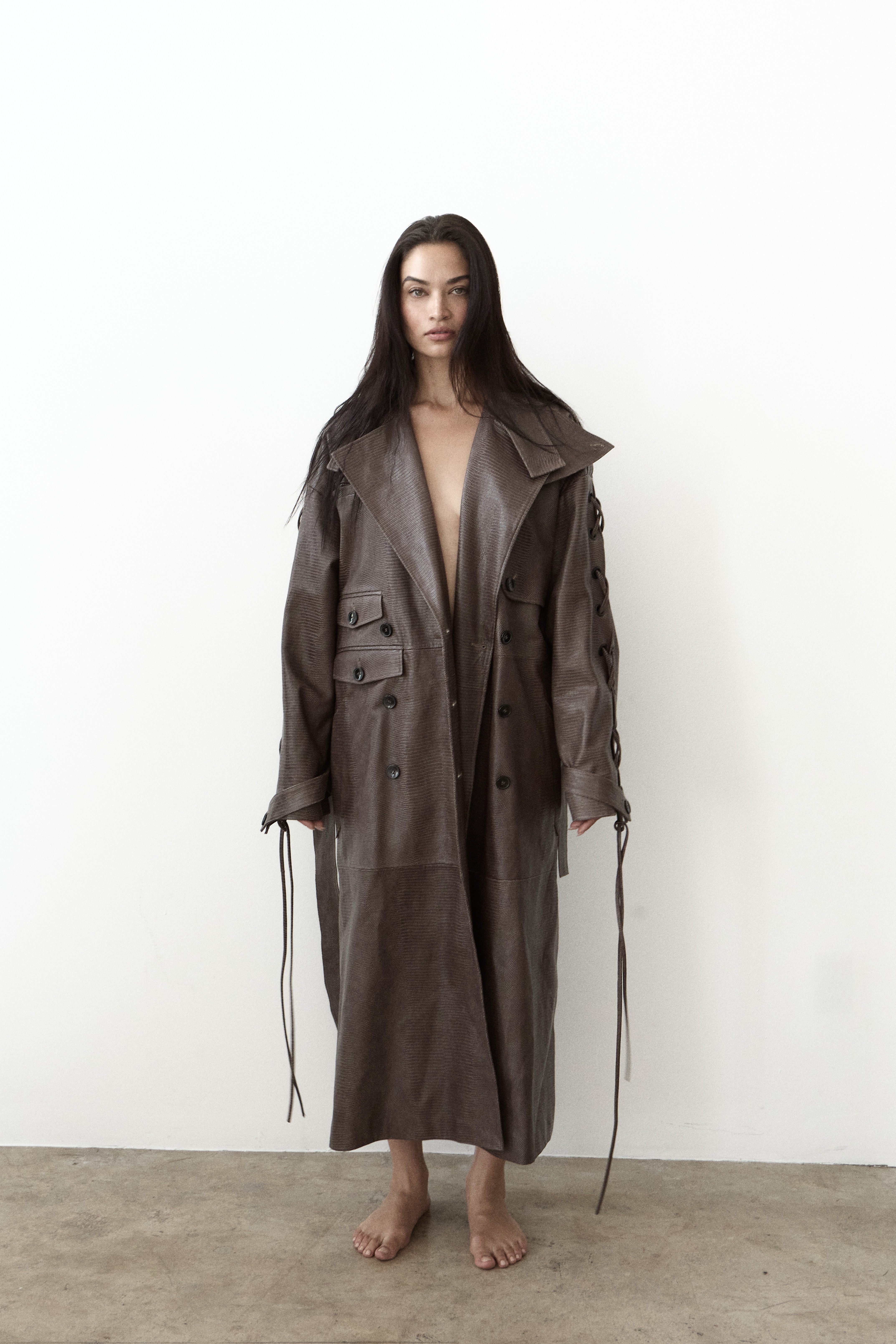 Woman in oversized olive double-breasted coat with tie details barefoot