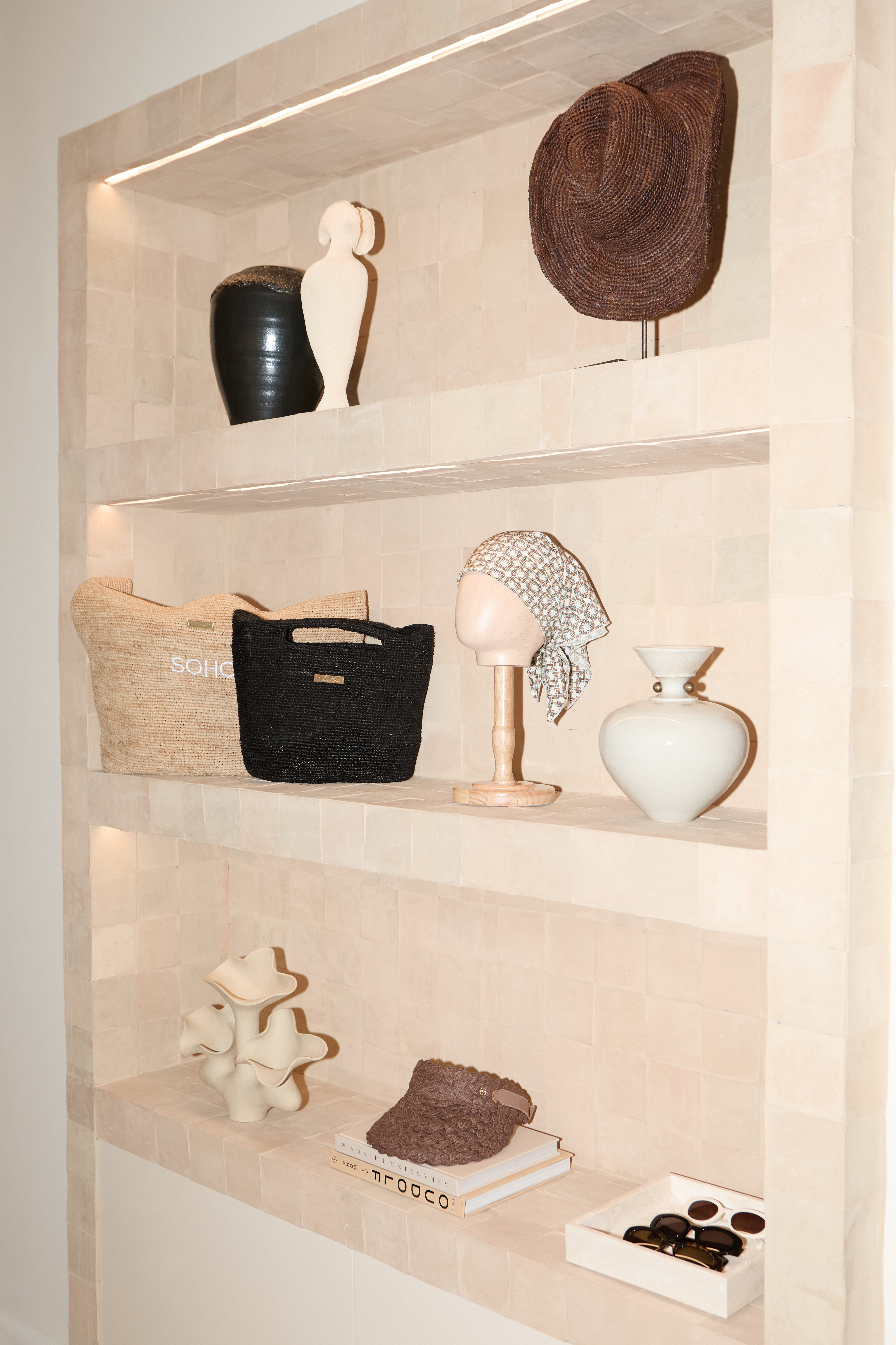 Styled retail shelf niche with vases, straw hats, woven bags, and sunglasses