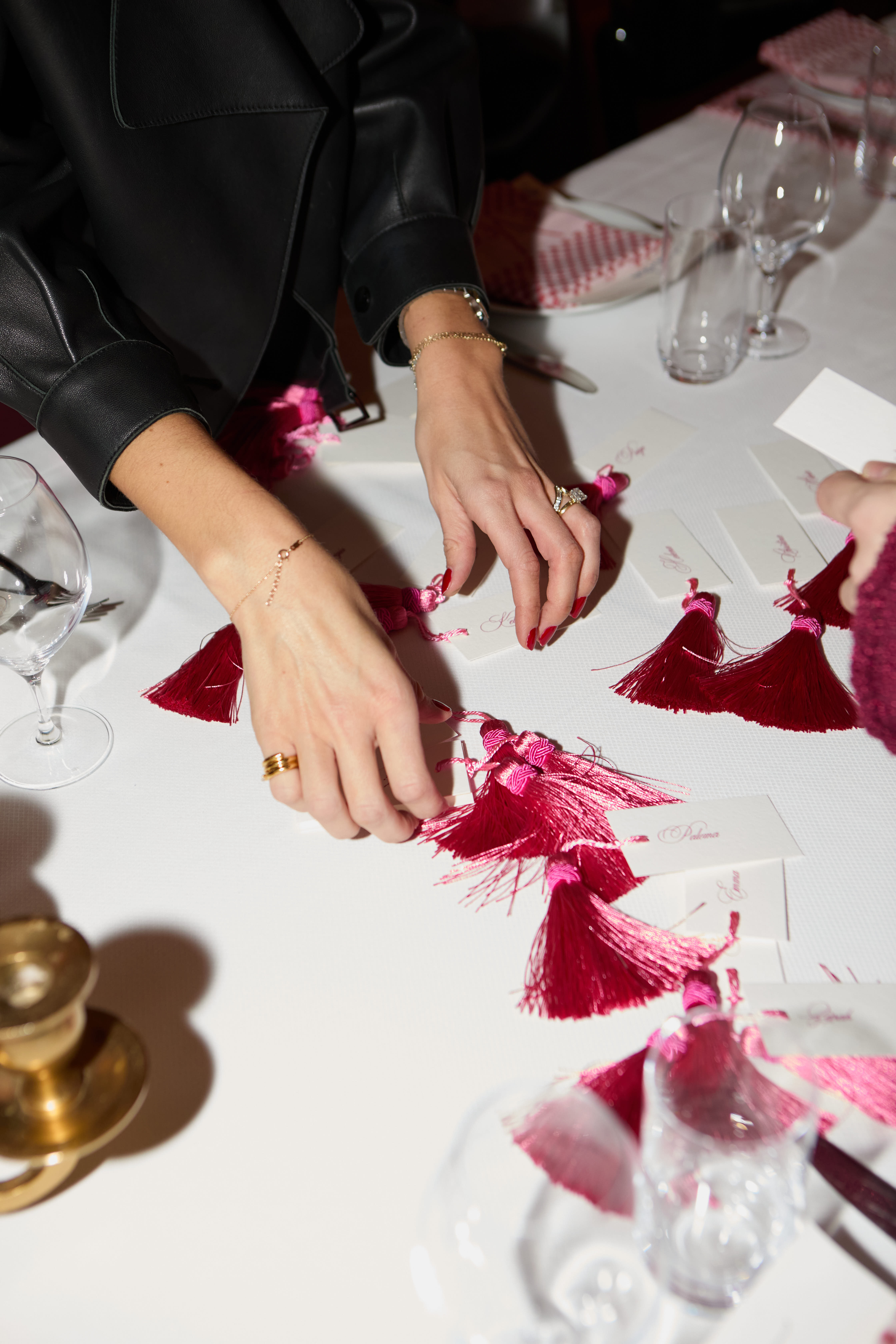 Hands arranging red and pink tasseled place cards on a white tablecloth