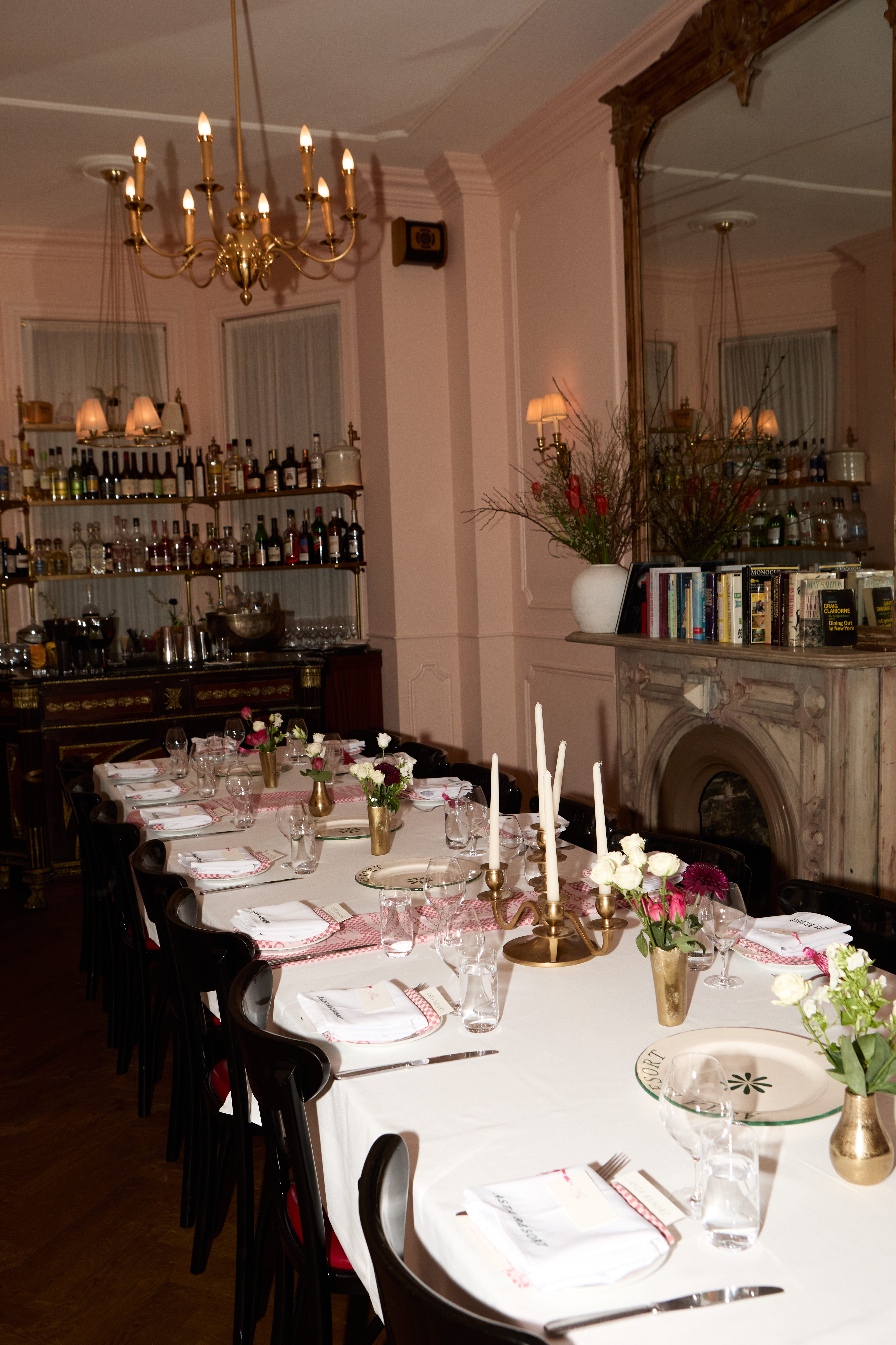 Pink-walled restaurant dining room with a brass chandelier, set tables, and candelabras