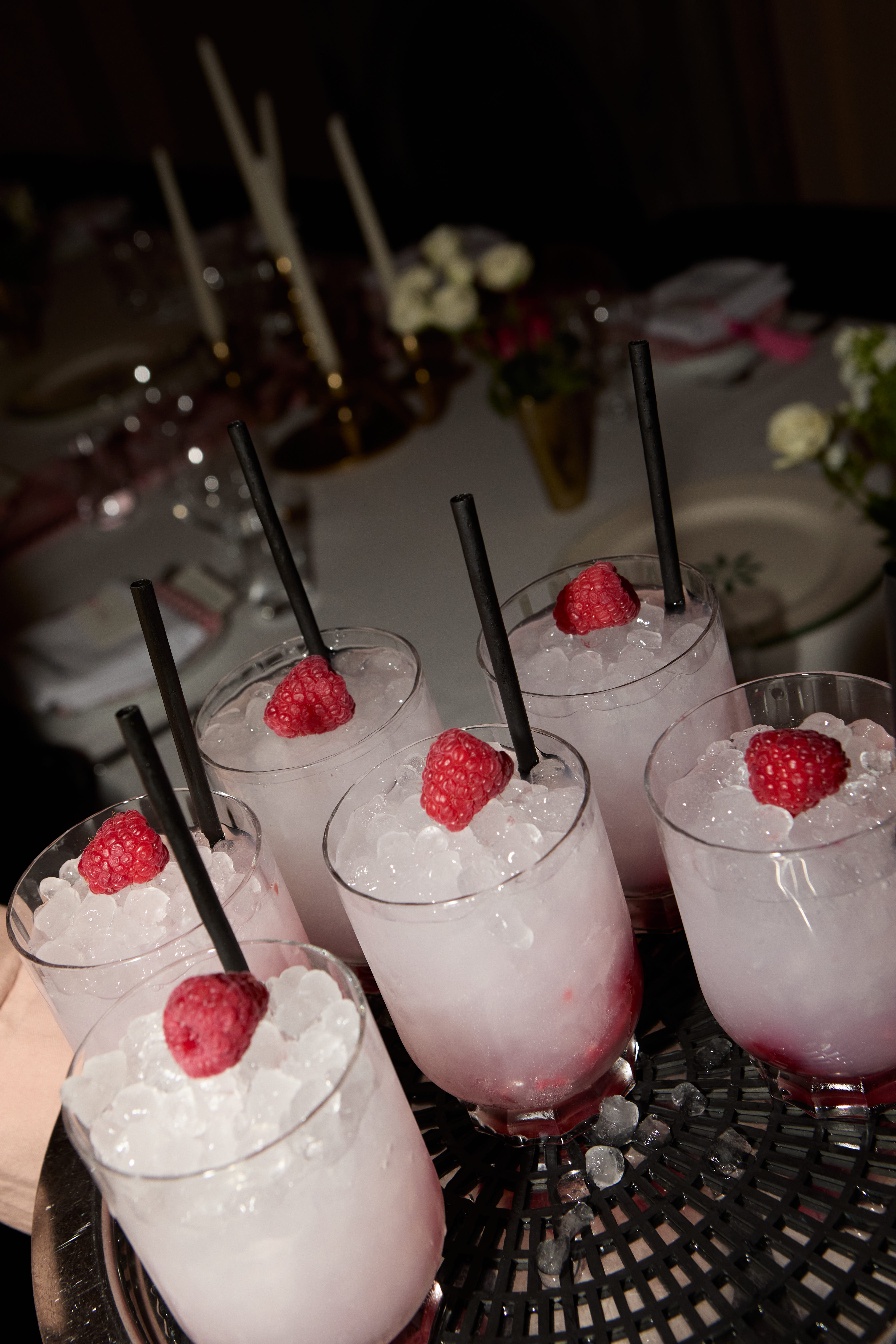 Tray of pink iced cocktails with raspberry garnishes and black straws at a candlelit table