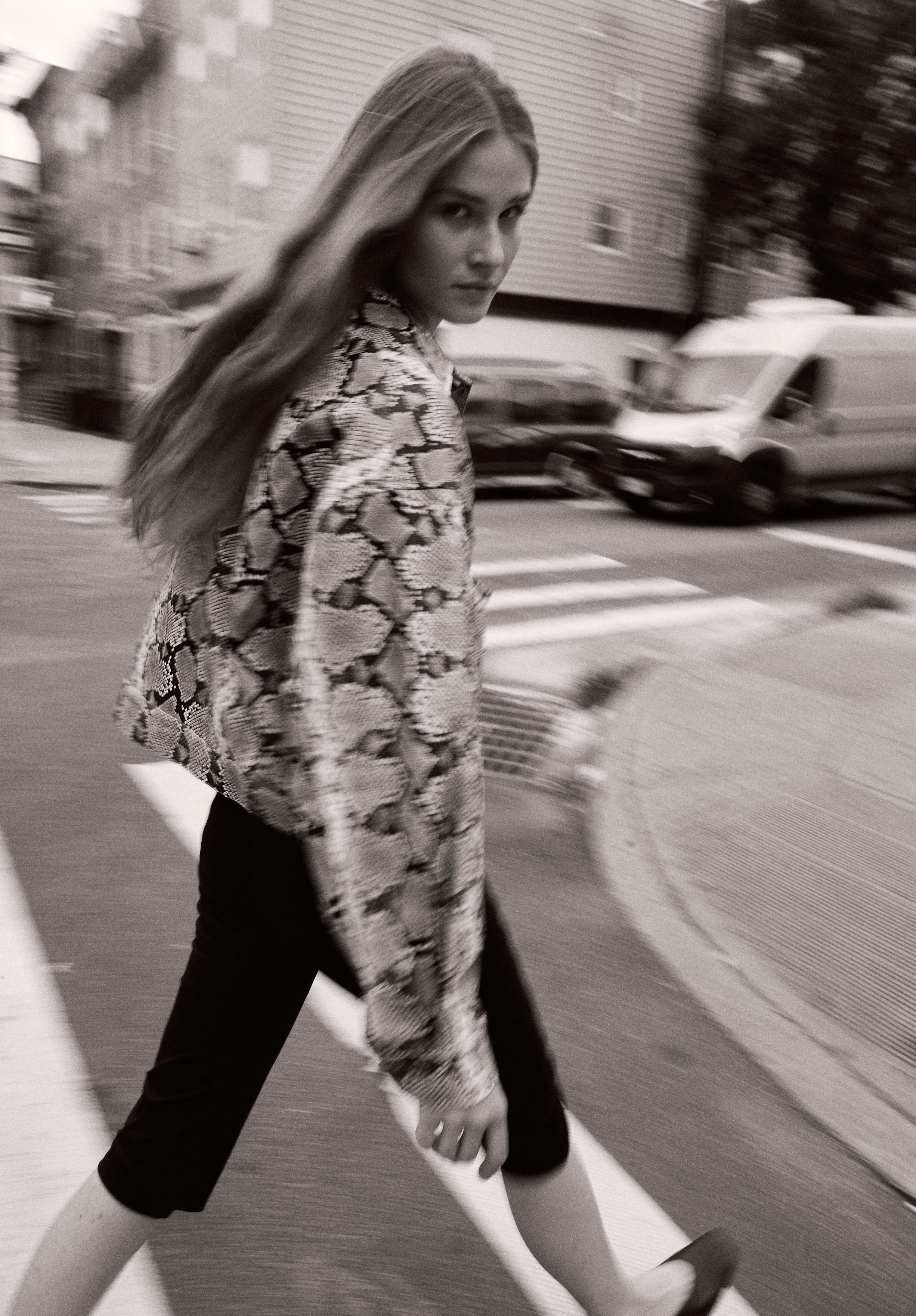 Black and white motion-blur street shot of a model in a snakeskin jacket crossing the road