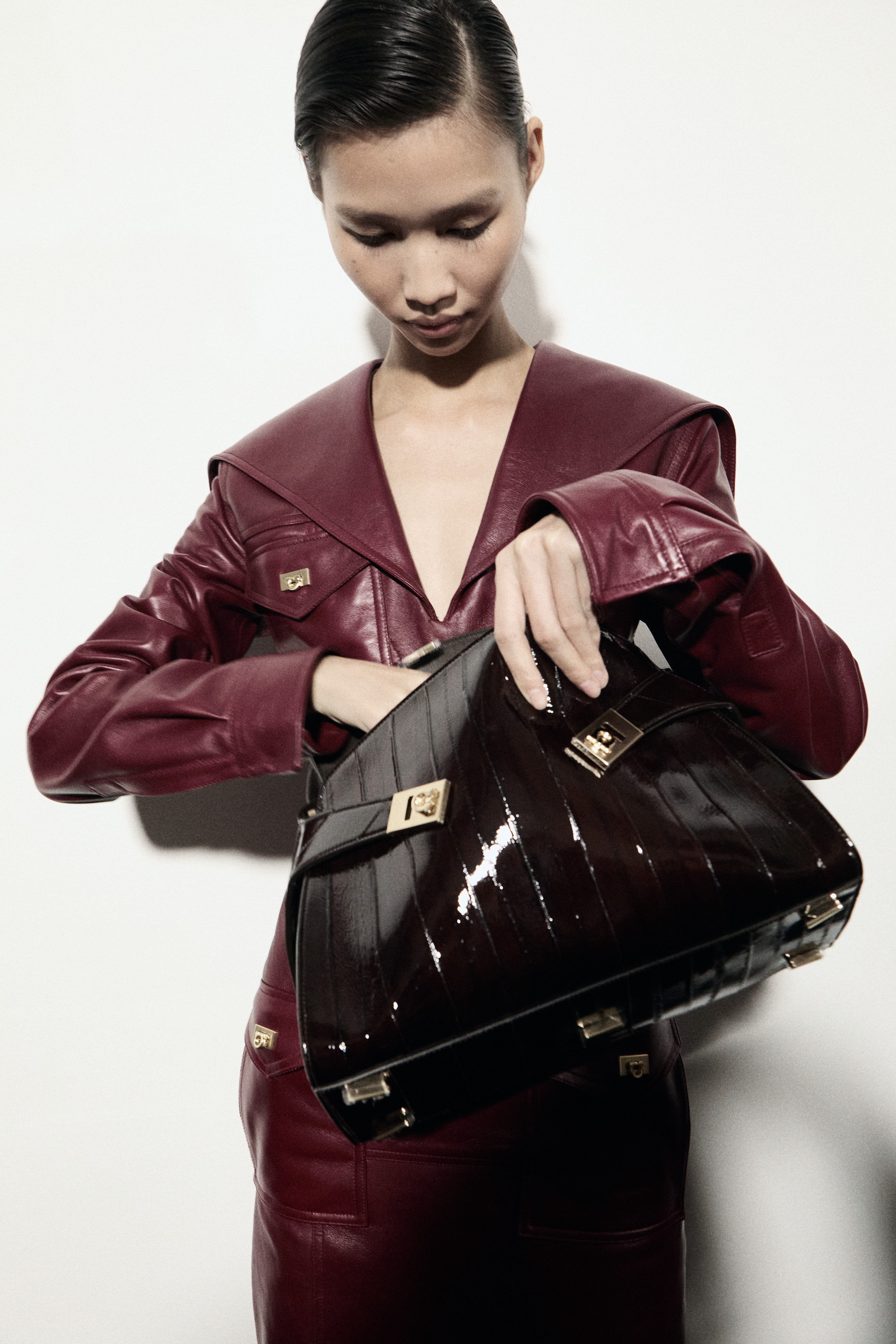 Woman in burgundy leather jacket holding black patent leather crocodile bag