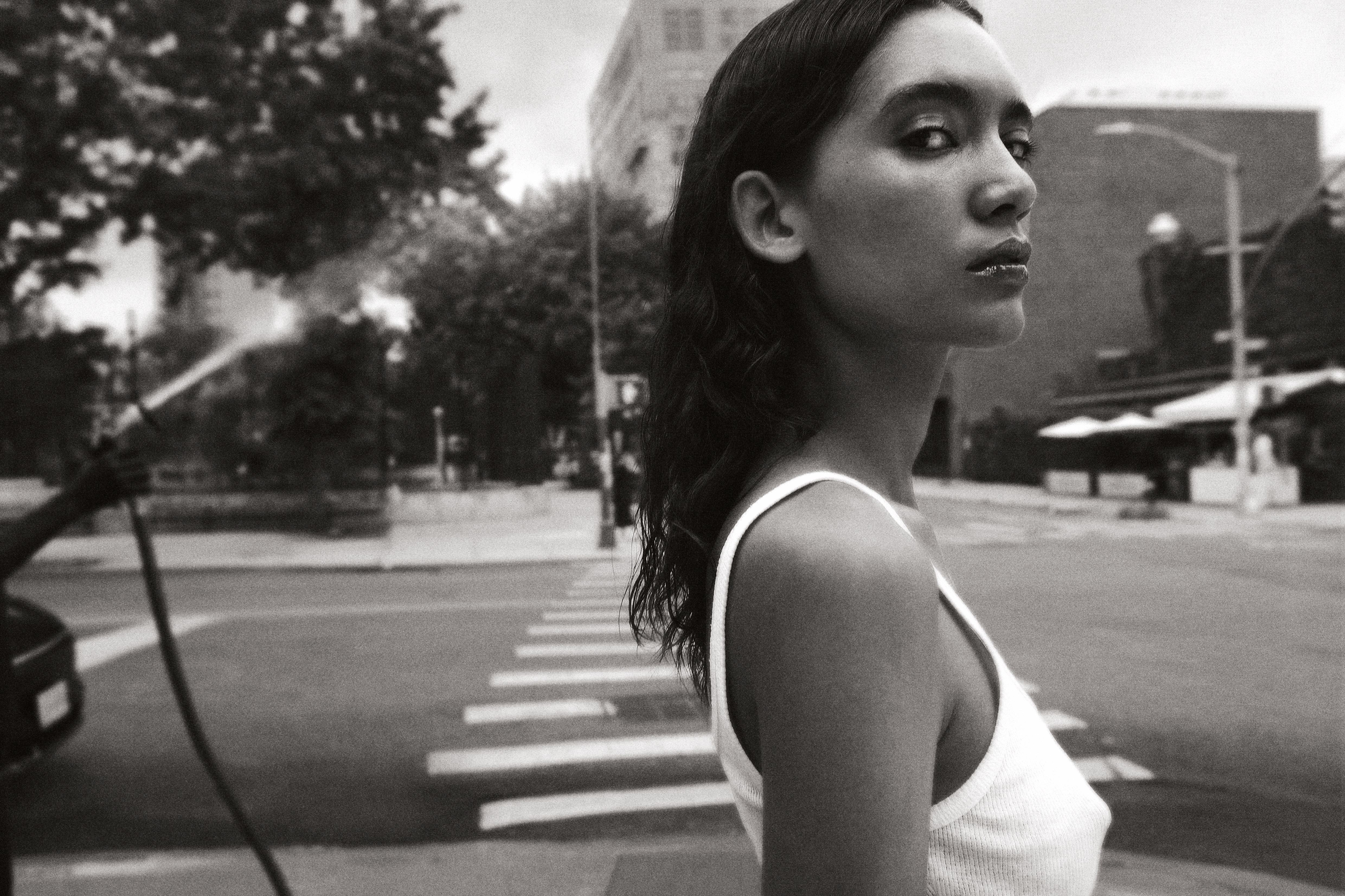 Black and white street portrait woman in white tank top at city crosswalk