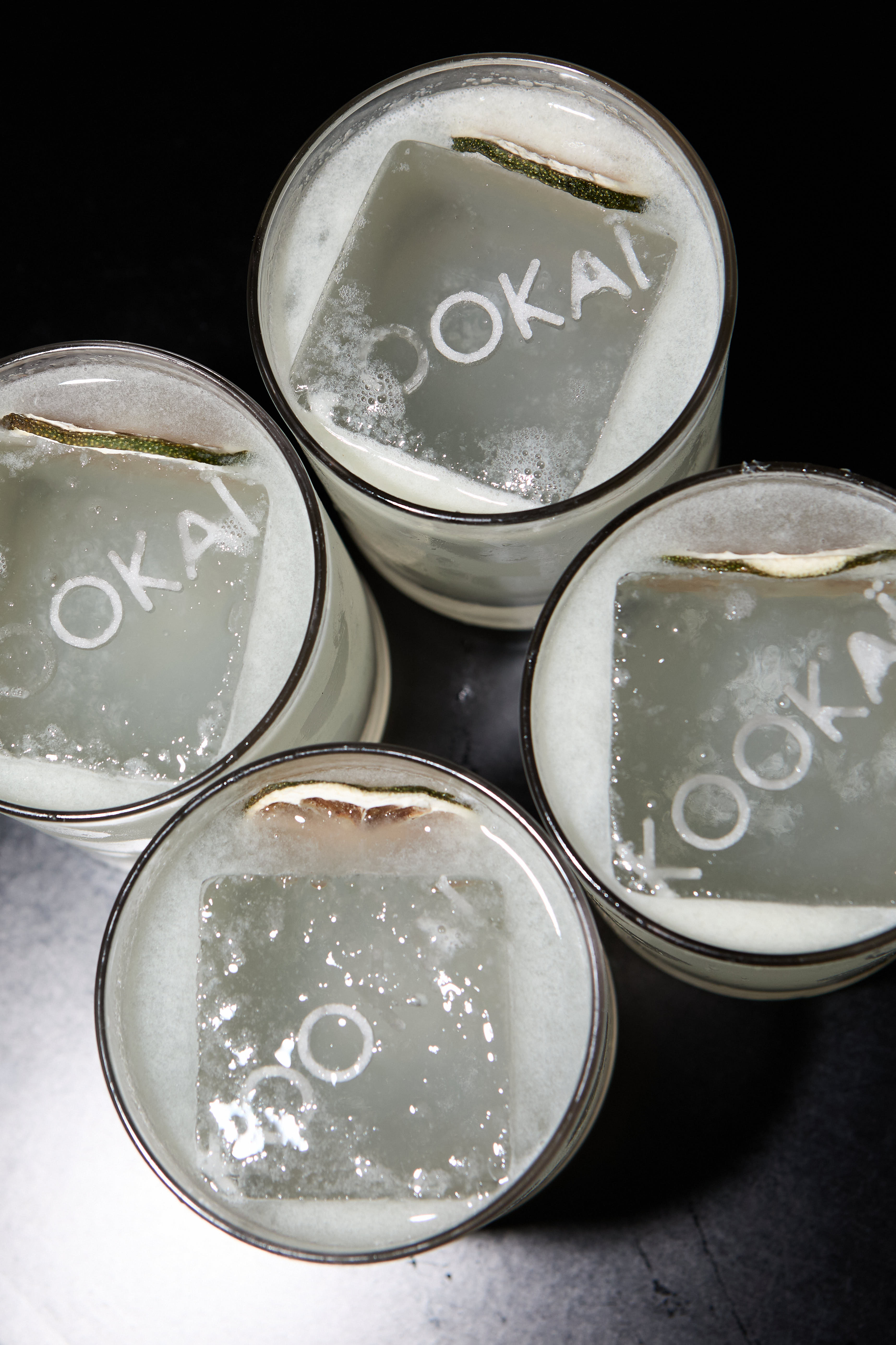 Overhead shot of four cocktails with KOOKAI-etched ice cubes on a dark surface