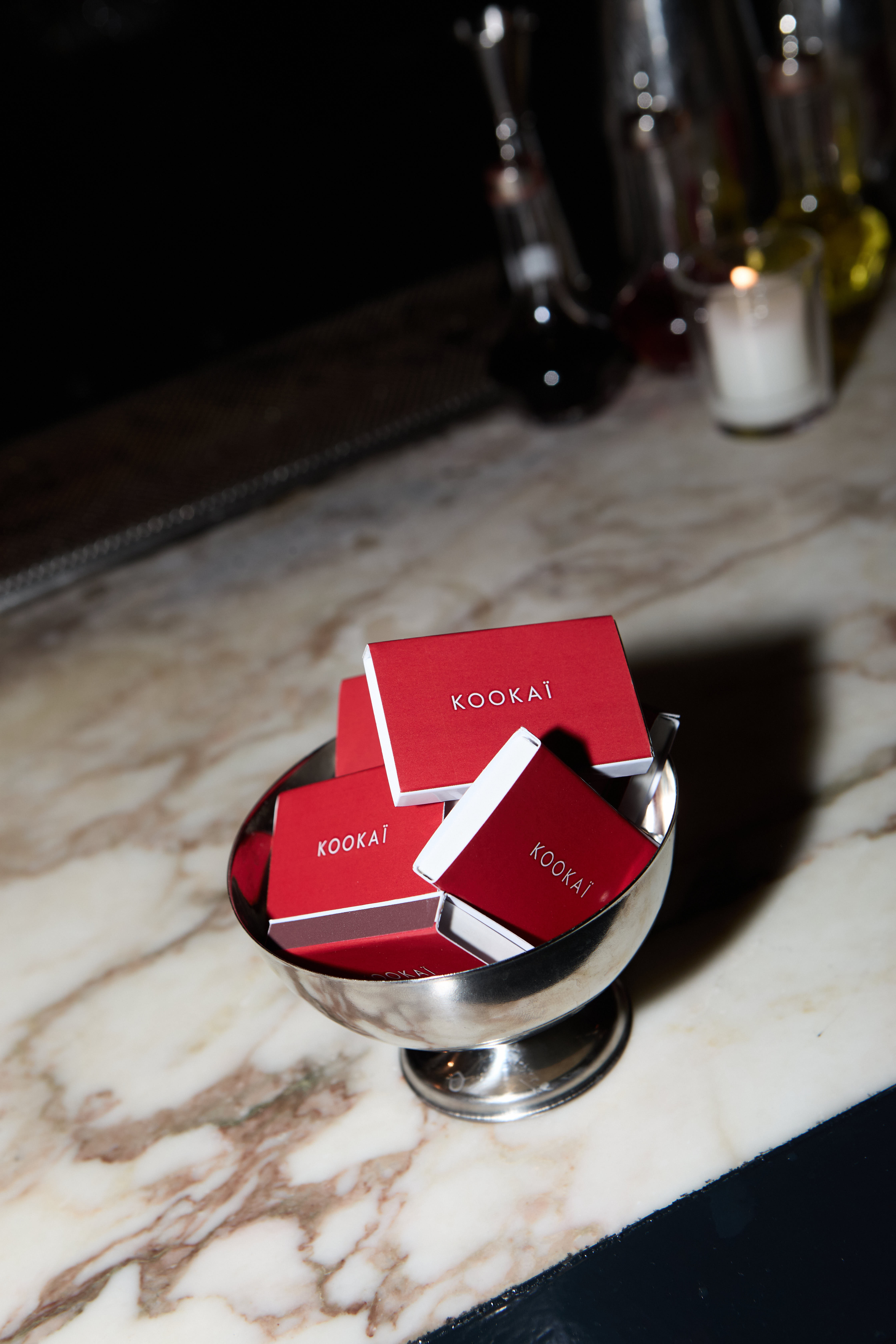 Silver pedestal bowl filled with red KOOKAI matchboxes on a marble bar
