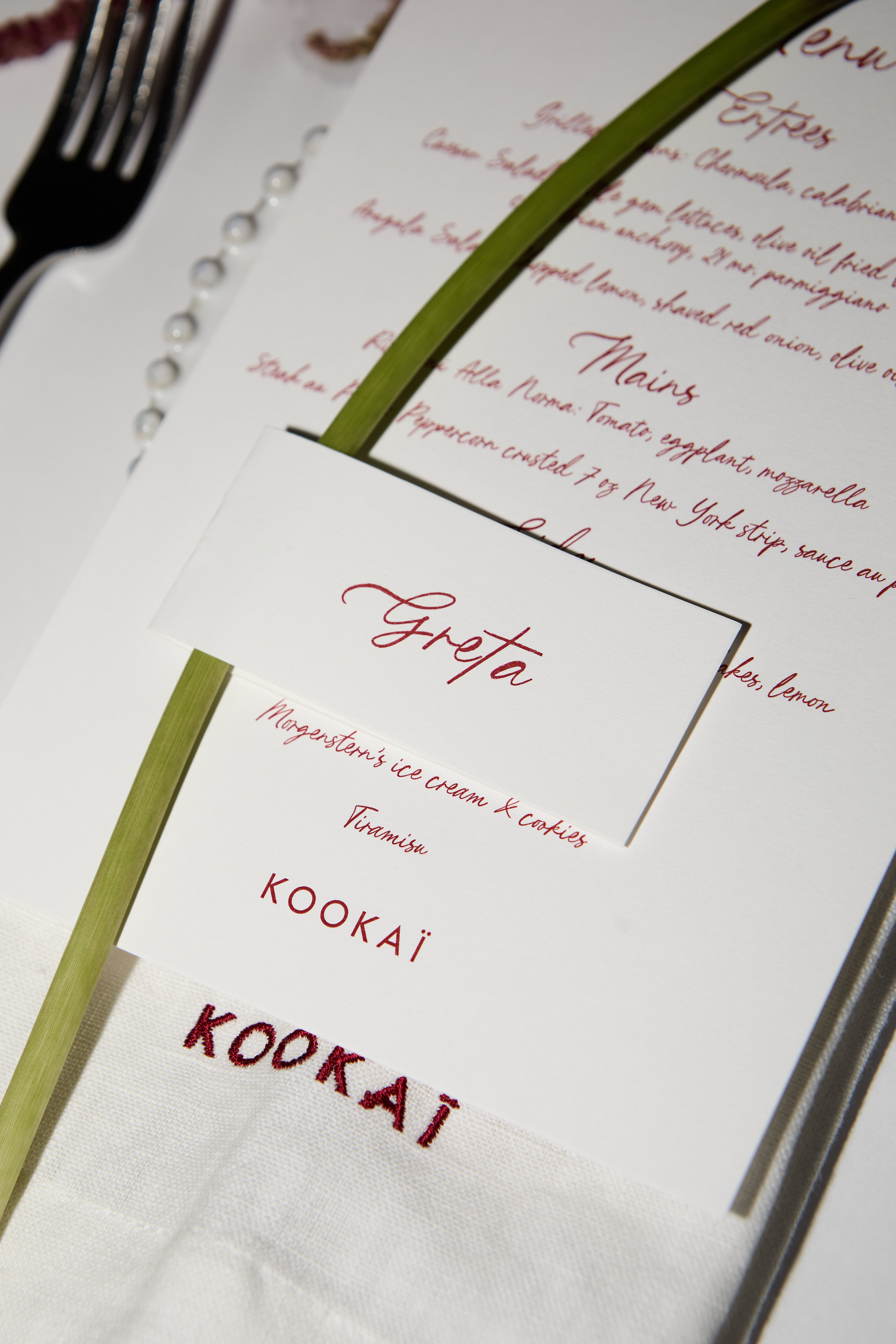Close-up of a KOOKAI menu and Greta place card on an embroidered napkin