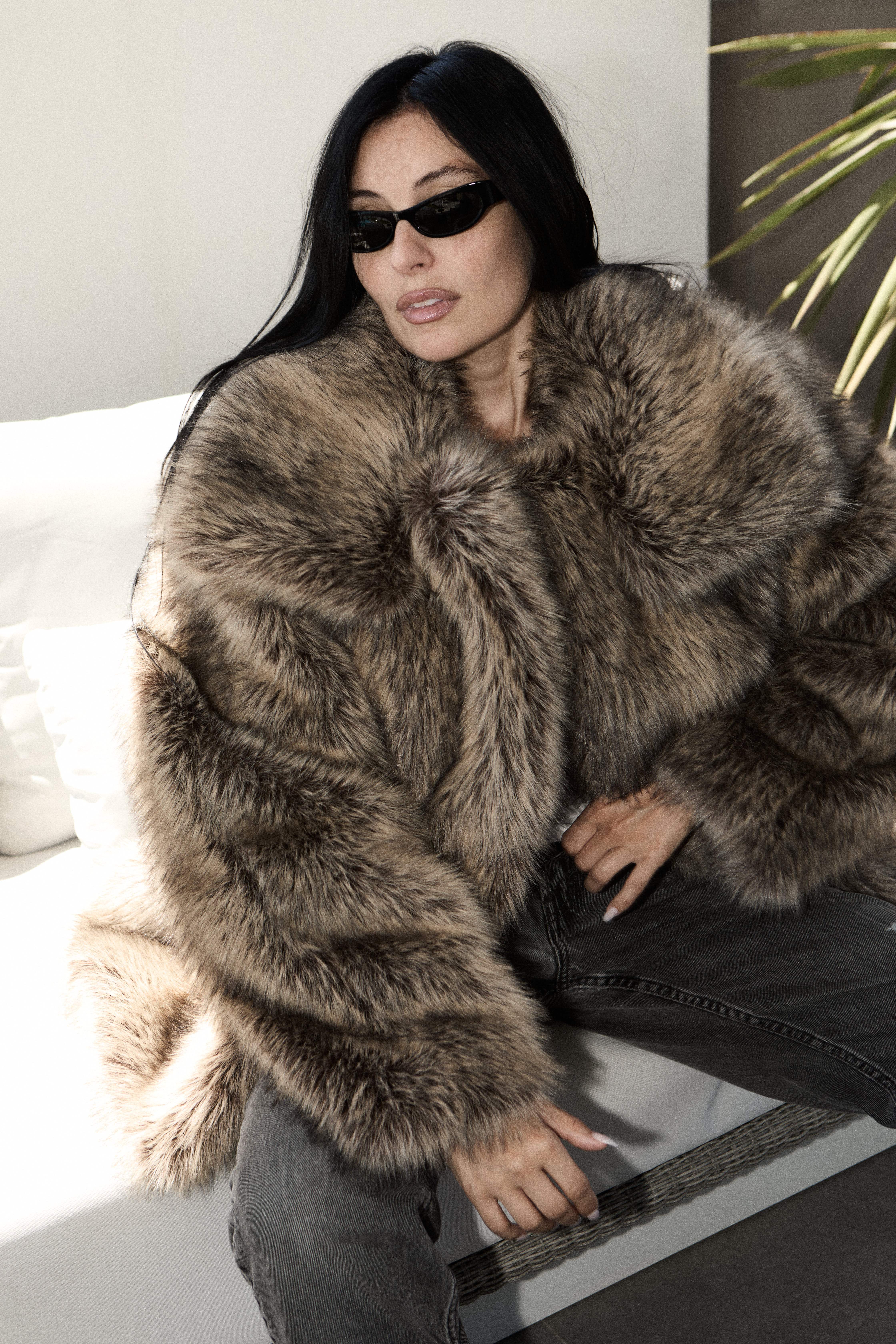 Woman in sunglasses and an oversized fur coat seated on a white couch