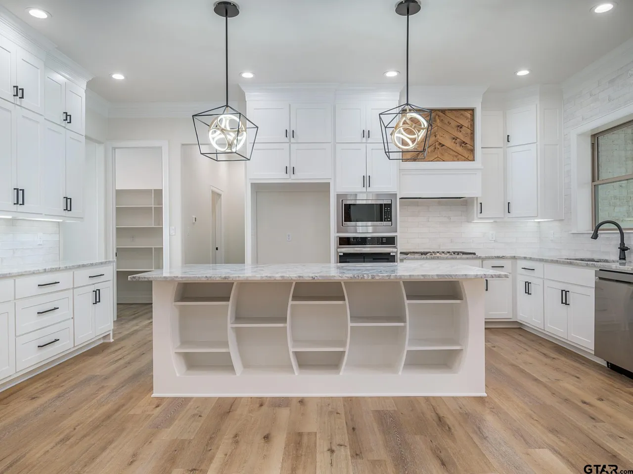 Large white kitchen with open-shelf island and geometric pendants