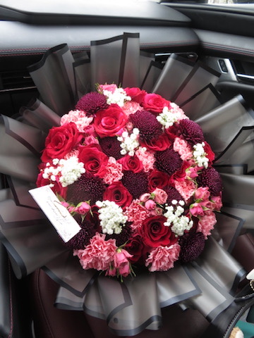 Red roses, burgundy dahlias, pink carnations and white baby's breath bouquet in black tulle wrapping inside car