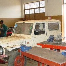 KFZ-Werkstatt: Jeep-Karosserie auf Böcken, Auszubildender im Hintergrund