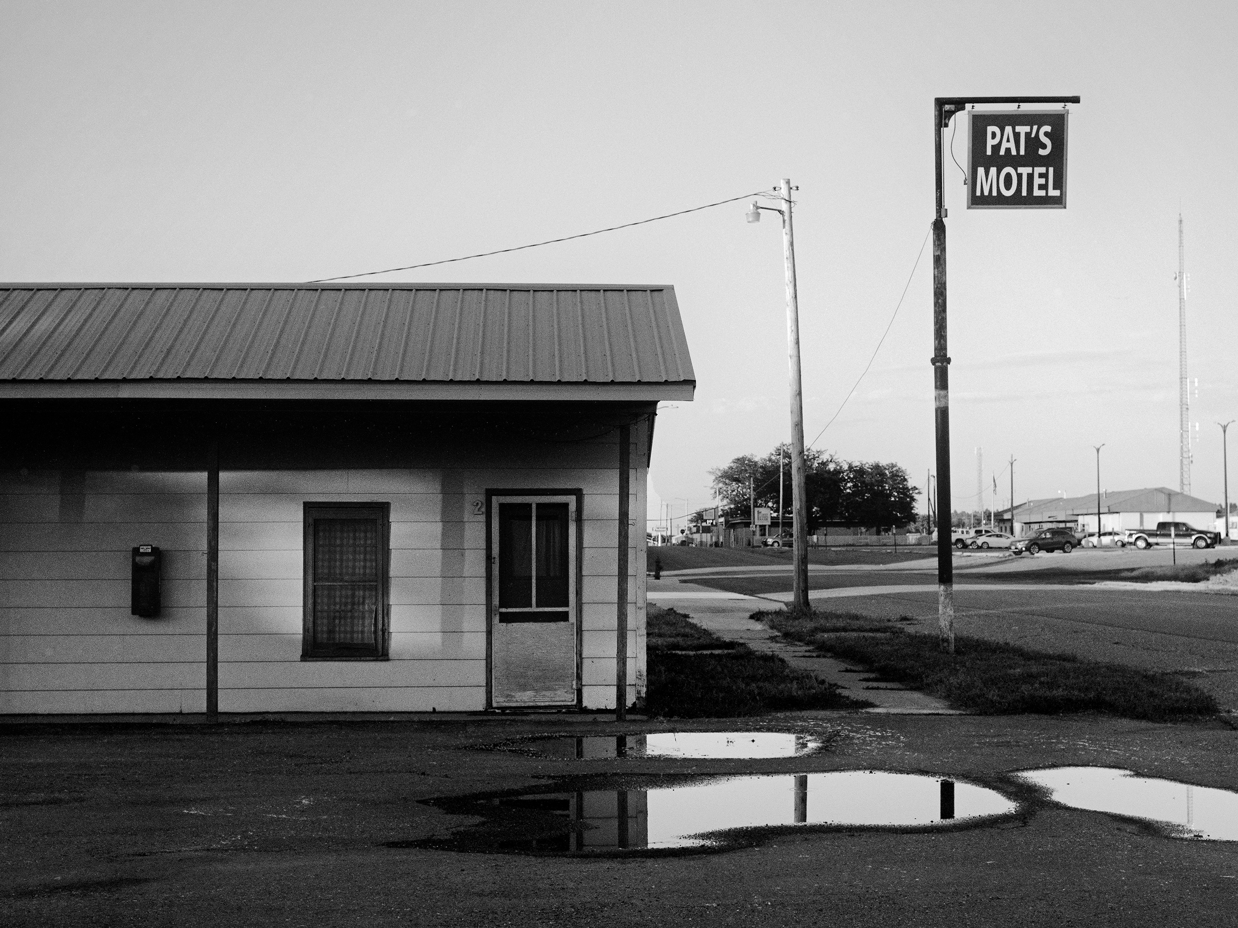 Pat's Motel with vintage sign and puddles reflecting in empty parking lot under overcast sky