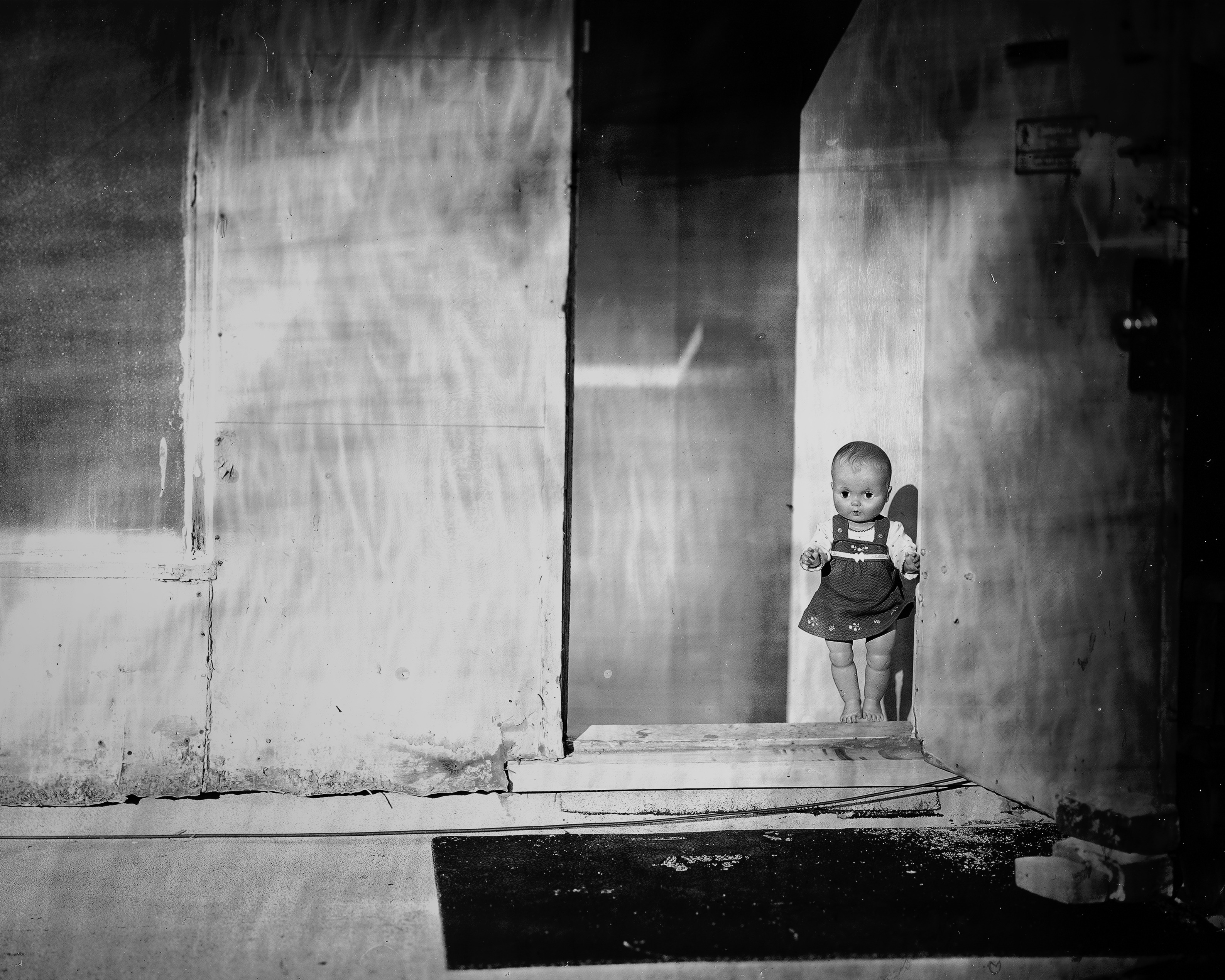 Child figure standing in doorway of severely deteriorated interior space with heavily weathered walls