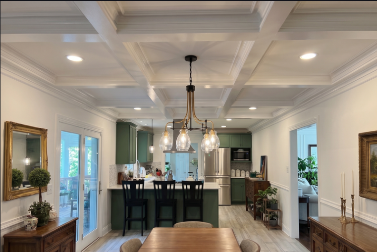 Open-concept kitchen and dining room with a white coffered ceiling, green cabinets, and a black chandelier