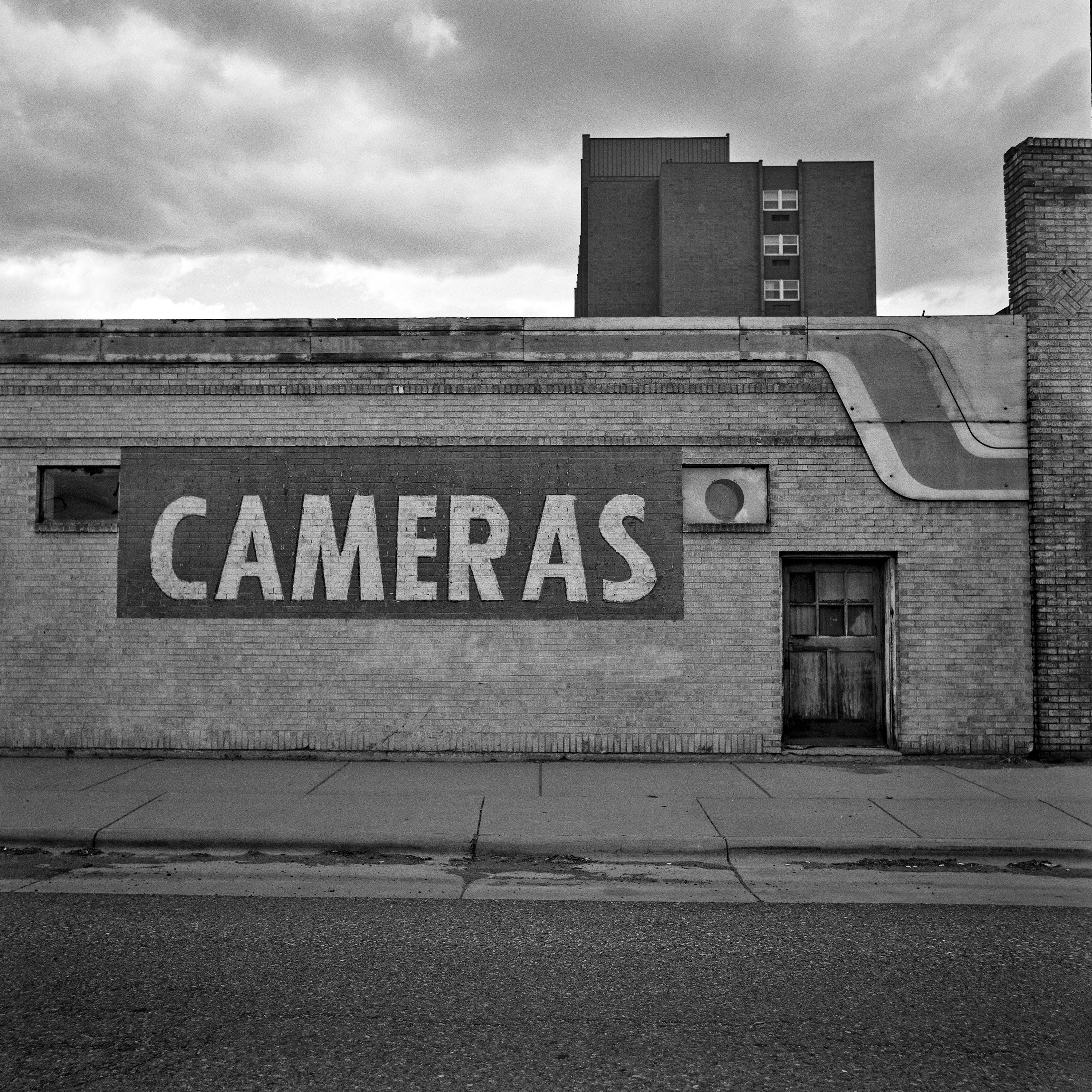 Faded CAMERAS painted sign on brick building with art deco architecture under stormy sky