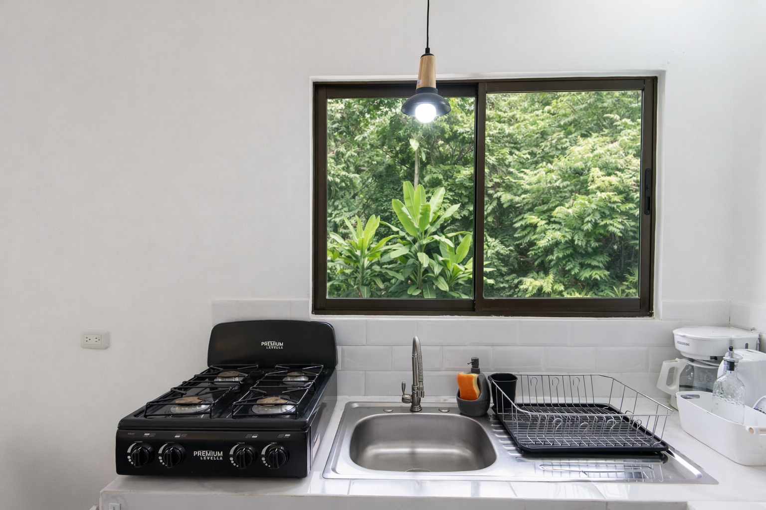 Kitchen close-up with gas stove, sink, jungle view window, pendant light
