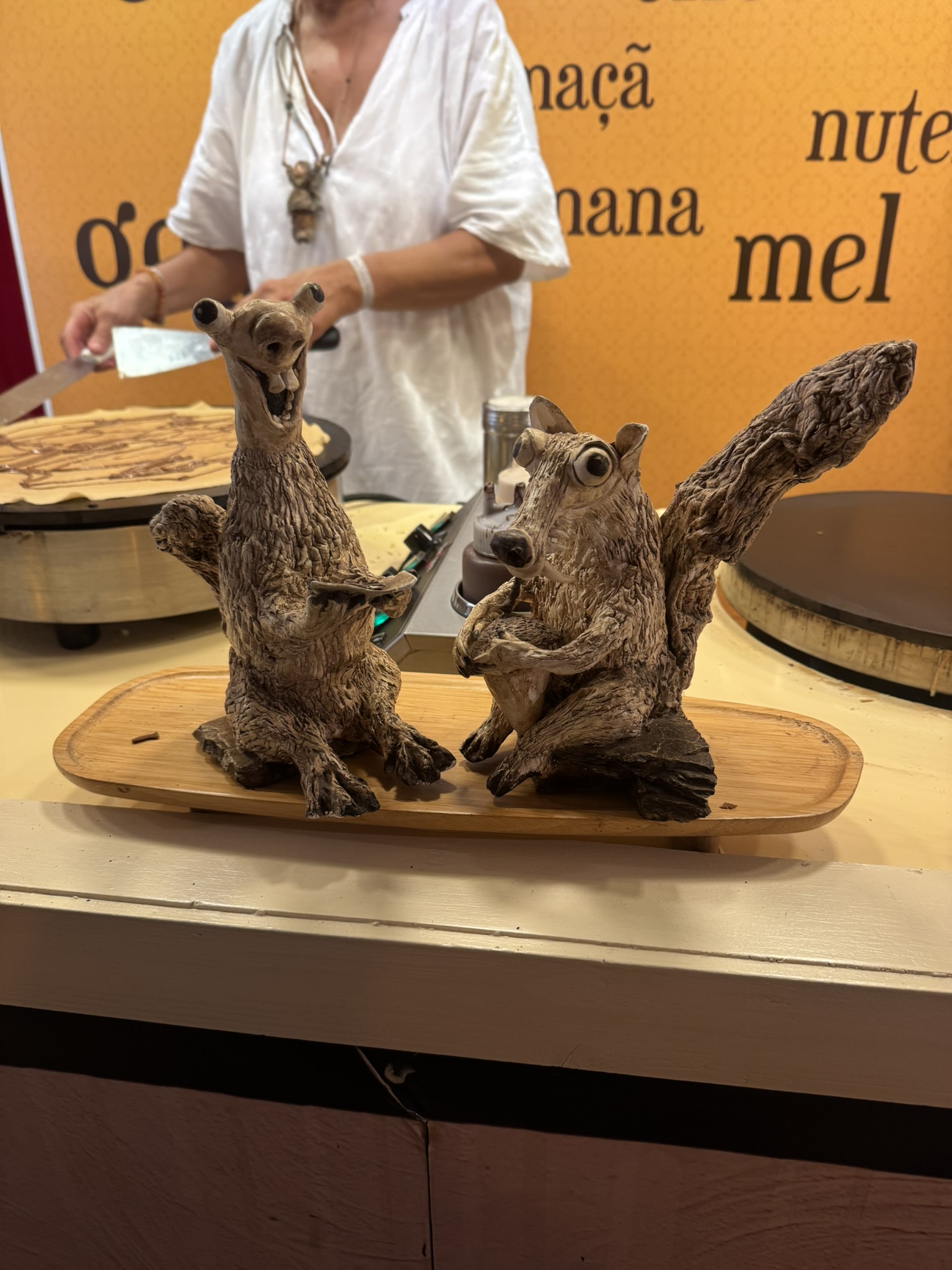 Two carved wooden squirrel sculptures on a board at a crepe stall
