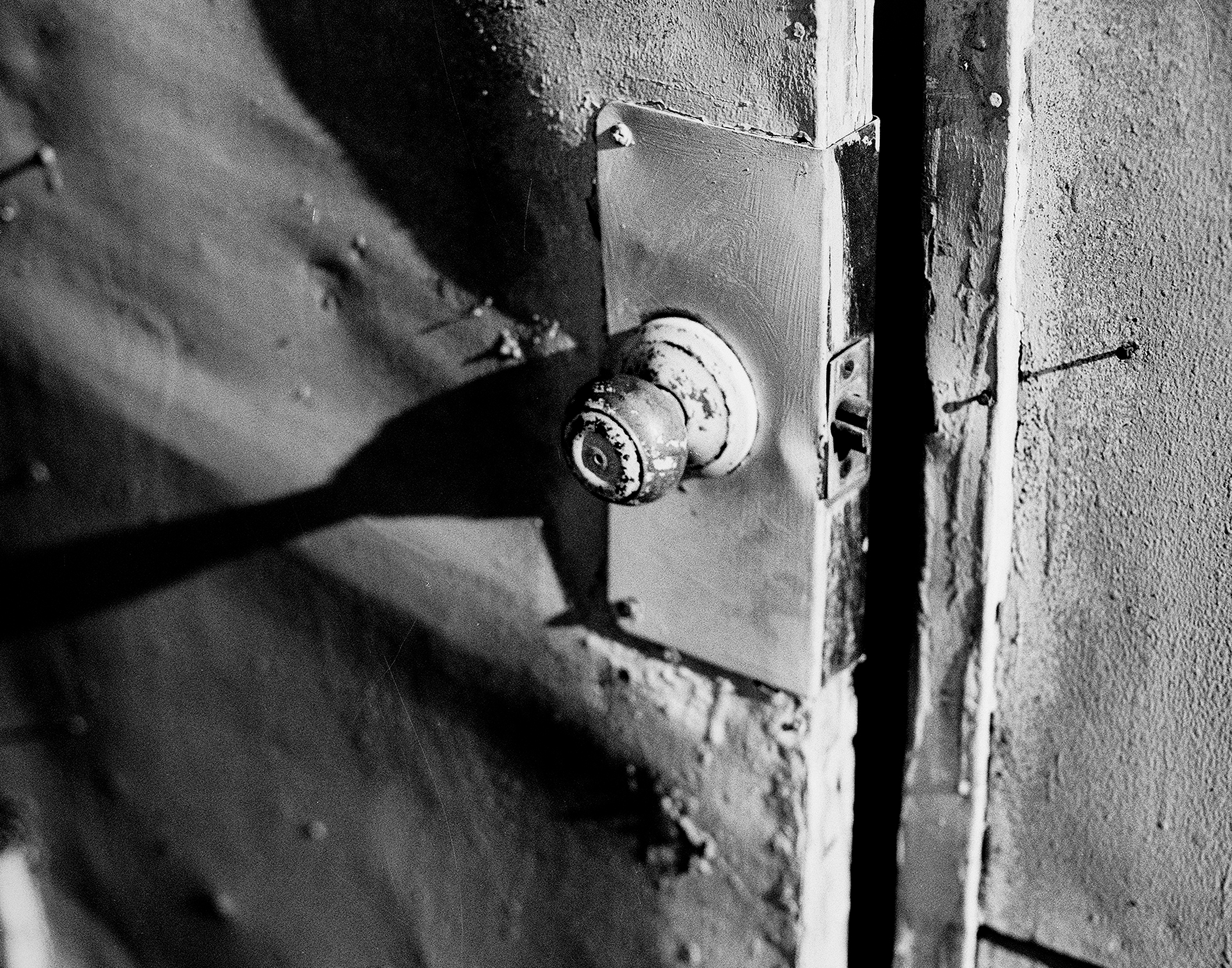 Dramatic close-up of weathered door knob and lock plate with textured patina on distressed urban door
