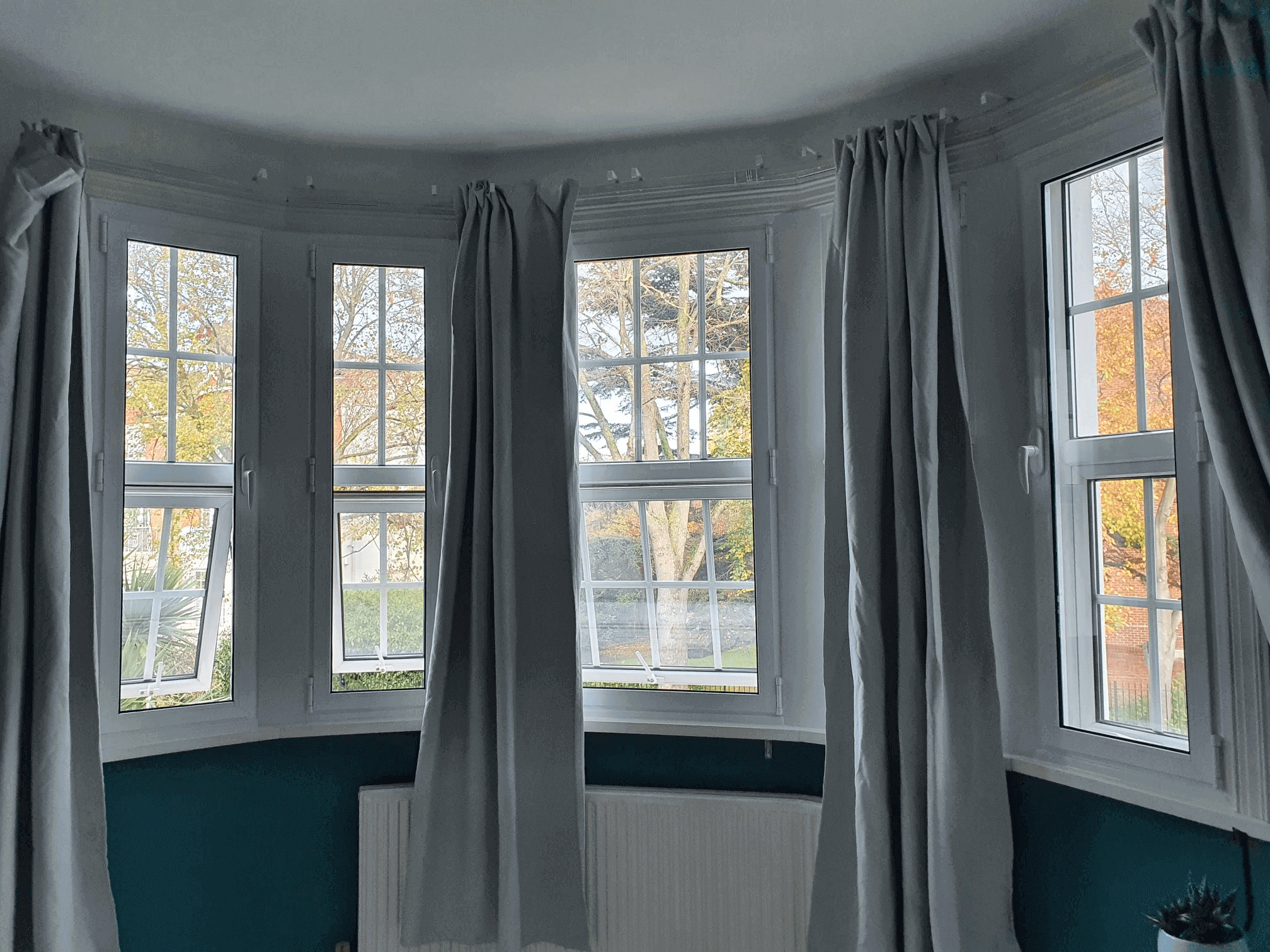 Curved bay window with secondary glazing and grey floor-length curtains in London Dulwich period property