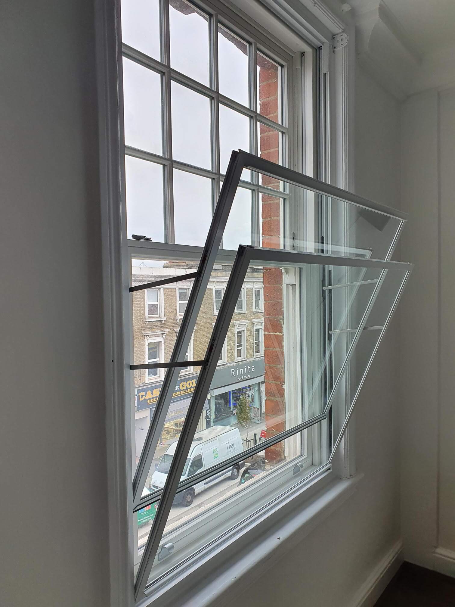 Hinged secondary glazing panel open on sash window showing lift-out mechanism for cleaning access in London Fulham property