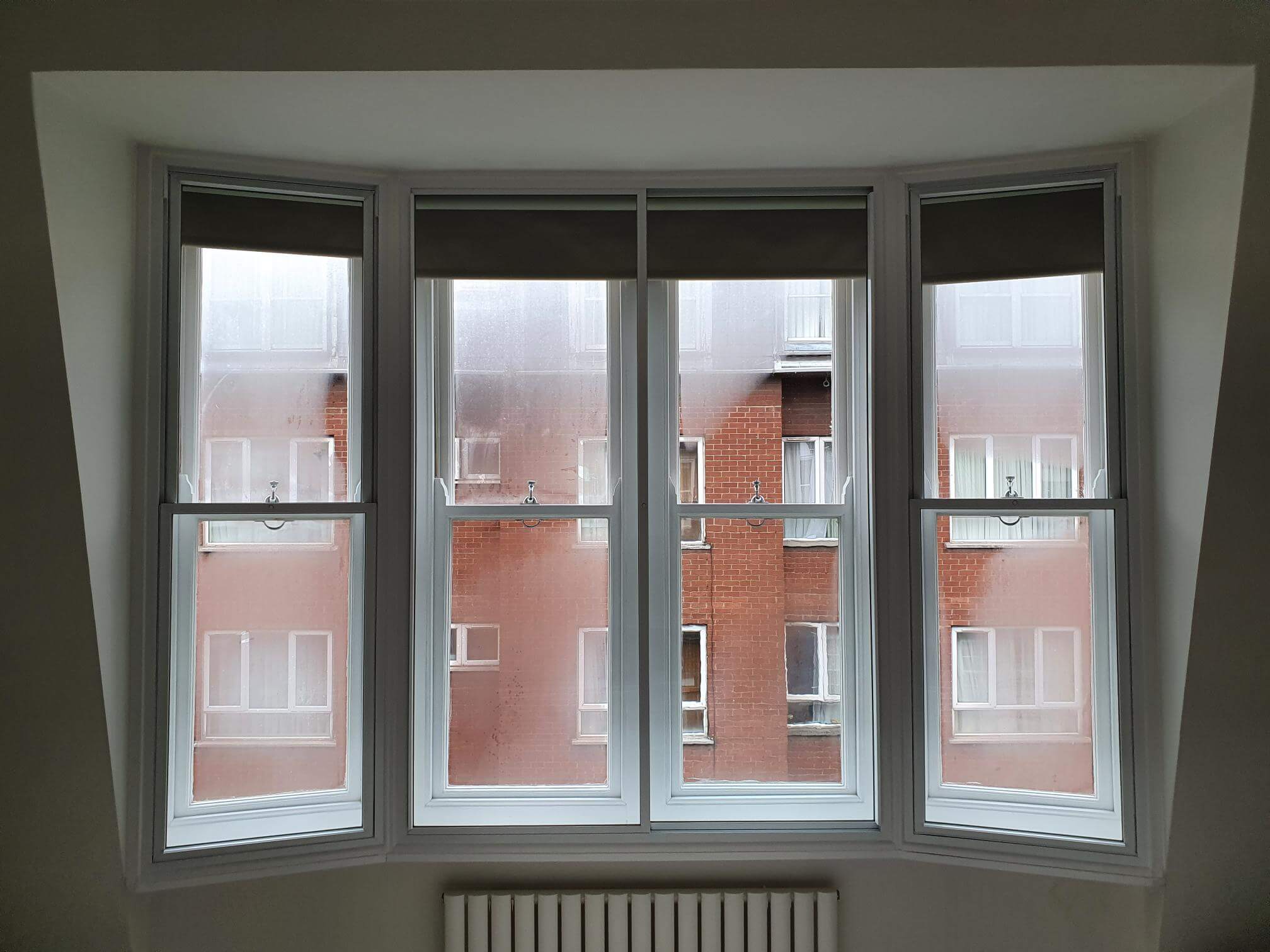 Four-panel bay window with sash secondary glazing and roller blinds in London Paddington flat
