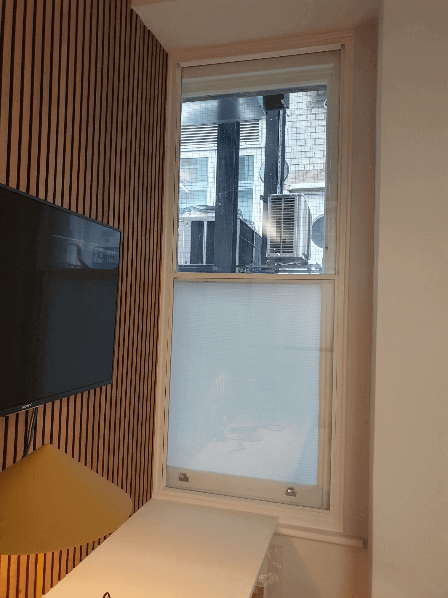 Sash window with frosted secondary glazing panel in modern London Soho interior with wood slat feature wall