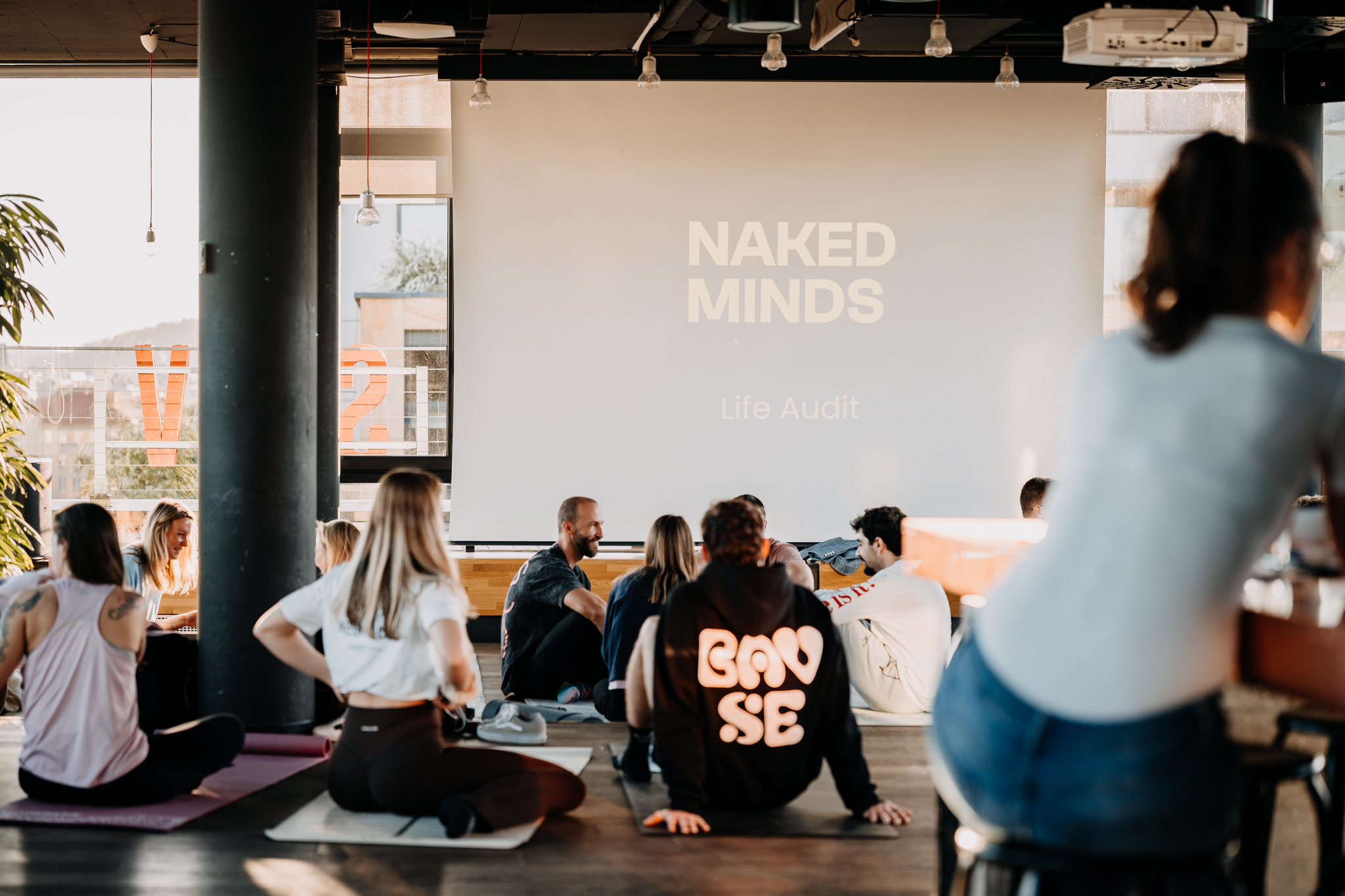 Group gathered on yoga mats in front of a Naked Minds screen