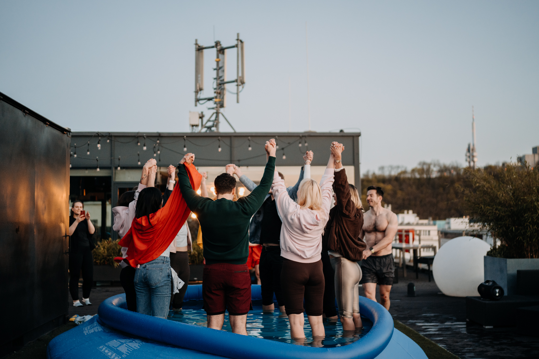 Participants raising hands together on a rooftop at sunset