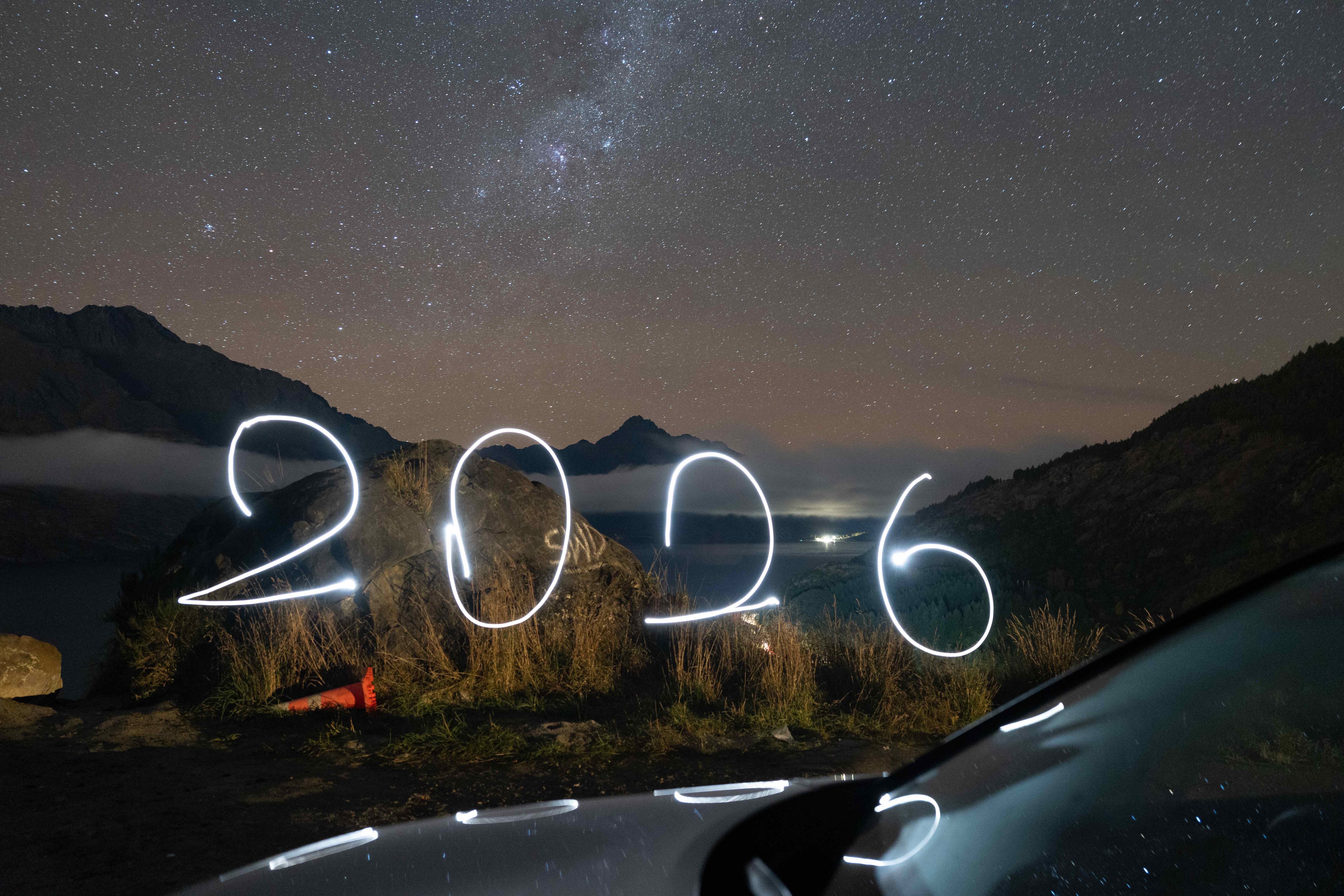 Light-painted 2026 under the Milky Way above a mountain lake at night