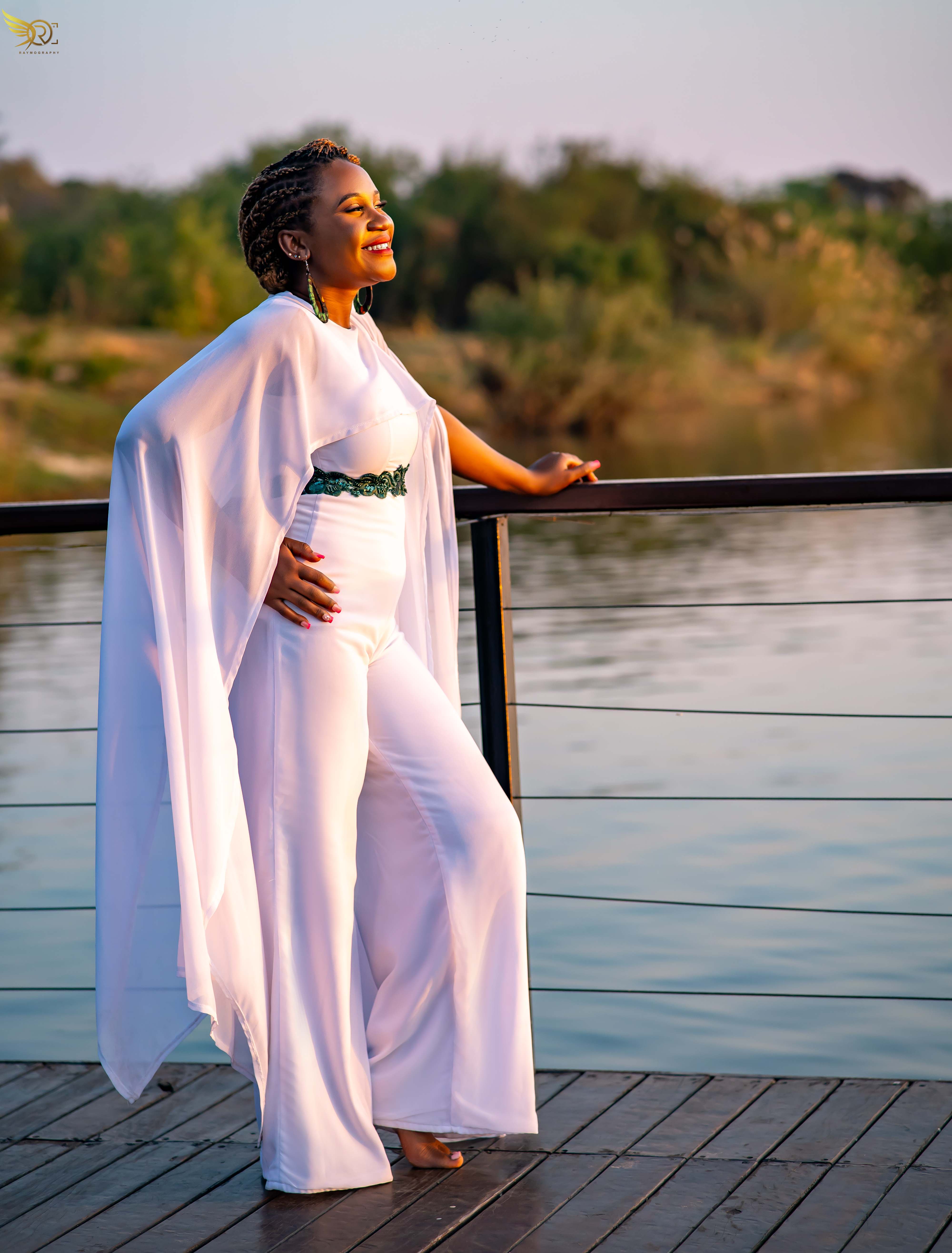 Tendai on wooden deck by water in flowing white outfit with sheer cape