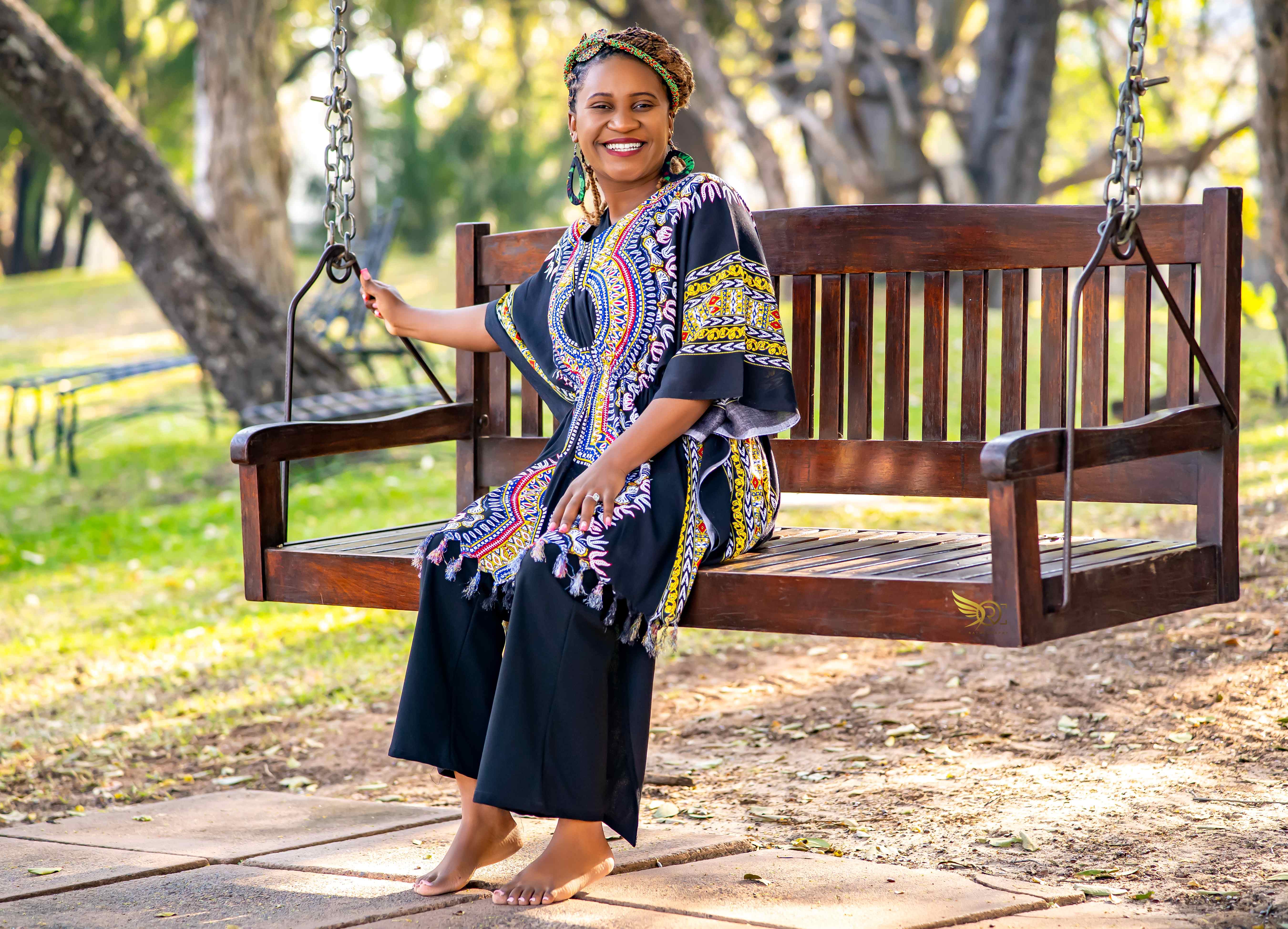 Tendai on swing wearing black outfit with colorful African print shawl in park setting