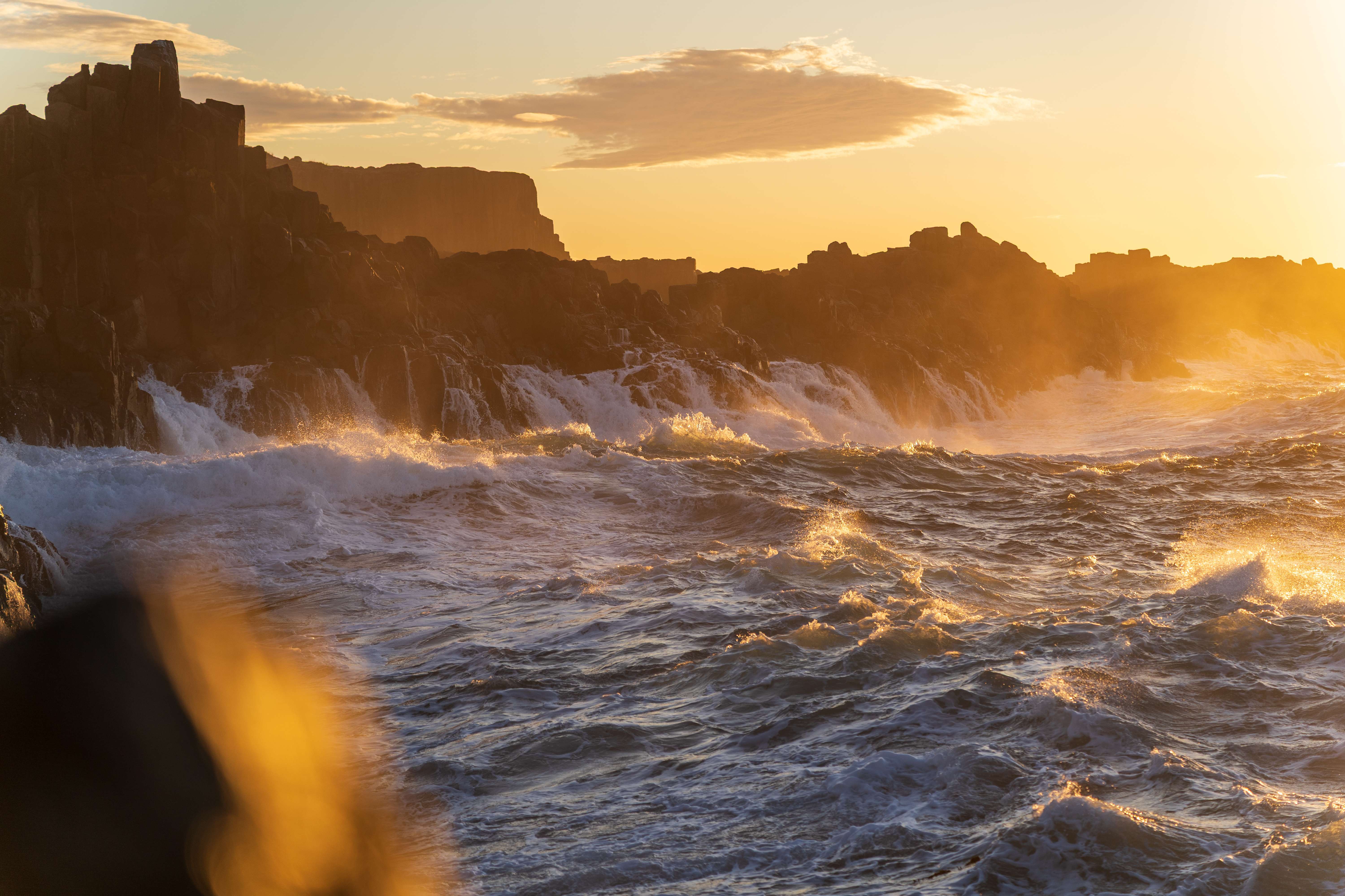 Dramatic waves breaking against cliffs at golden sunrise