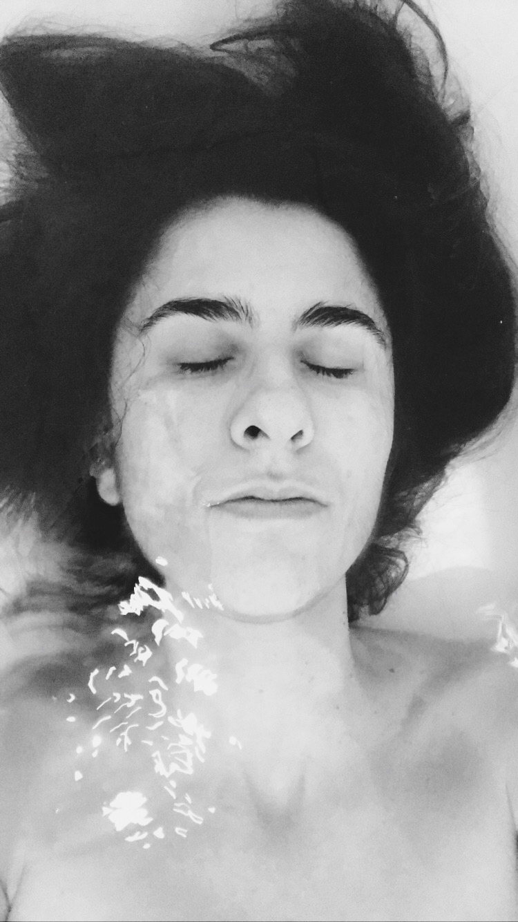 Black and white self-portrait of a woman with curly hair in water, eyes closed