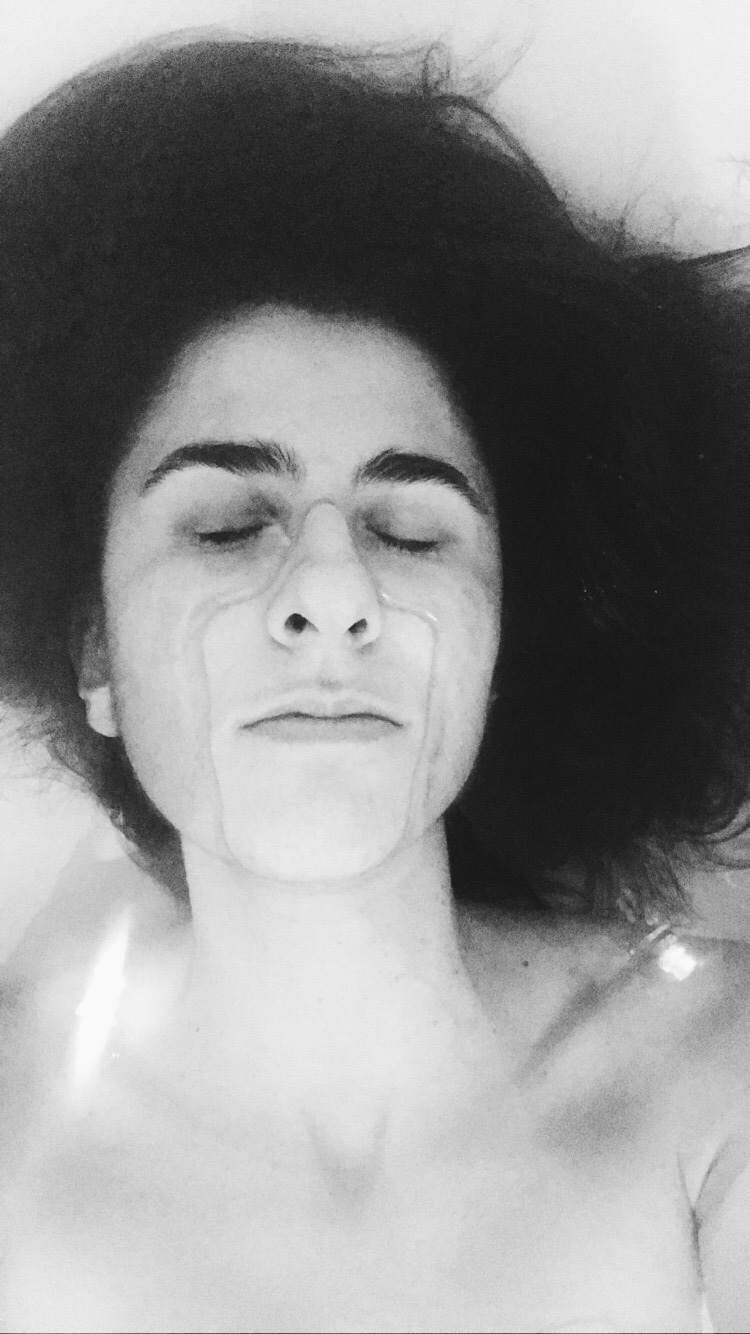 Black and white close-up self-portrait of a woman with curly hair in water