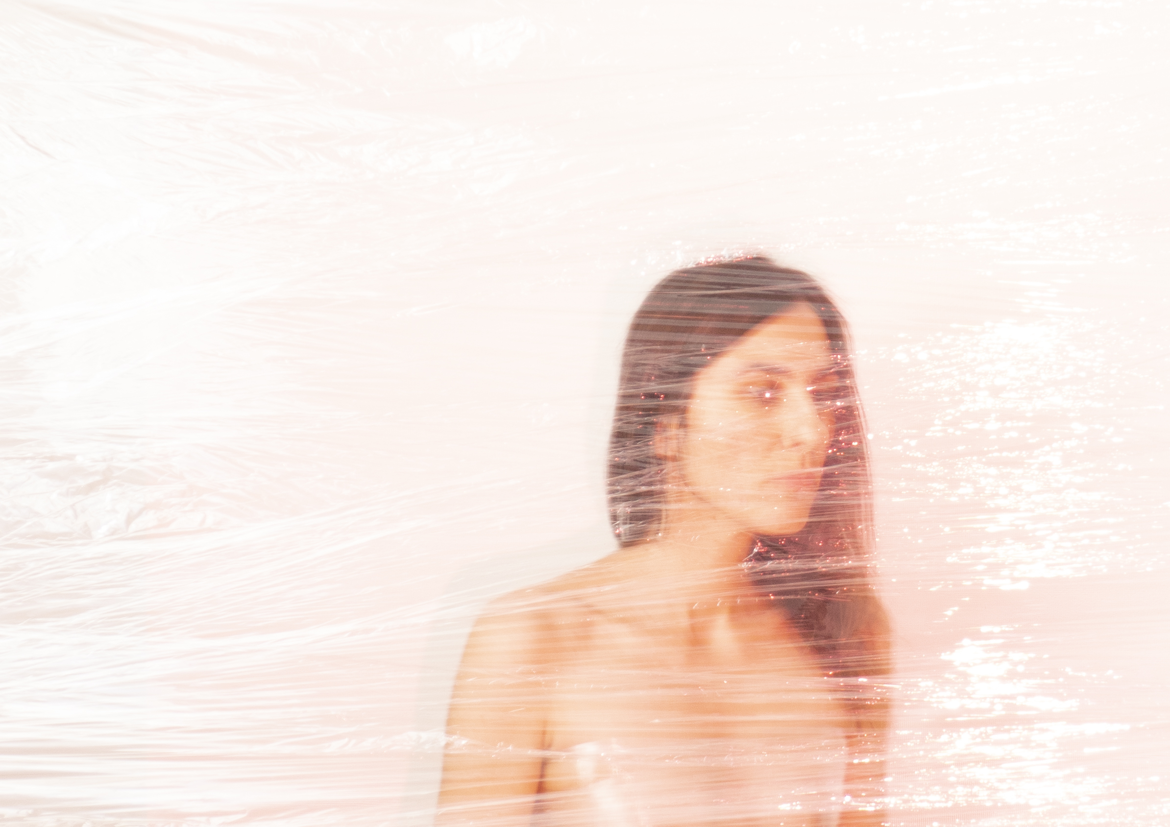 Ethereal self-portrait with pinkish hue showing a partially visible figure behind a textured surface