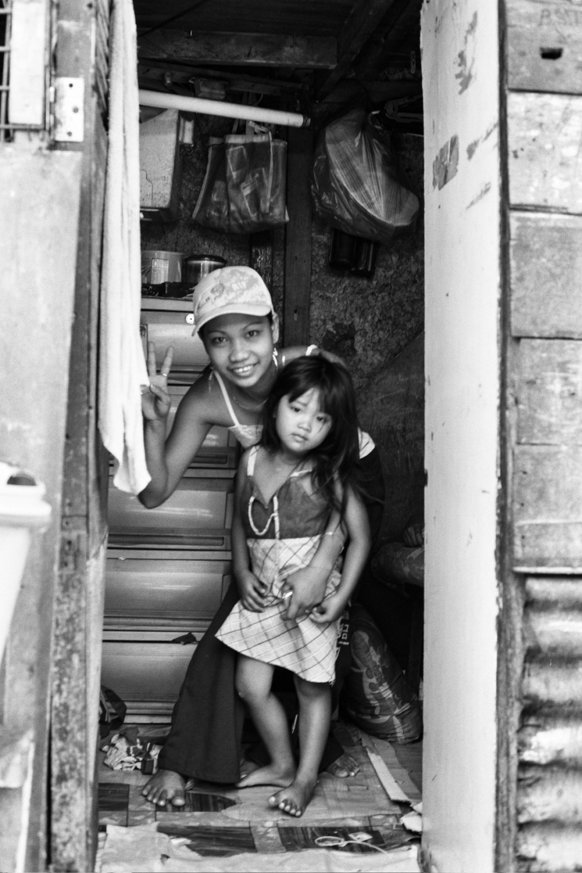 Young woman and child smiling from inside modest dwelling viewed through doorway with hanging laundry