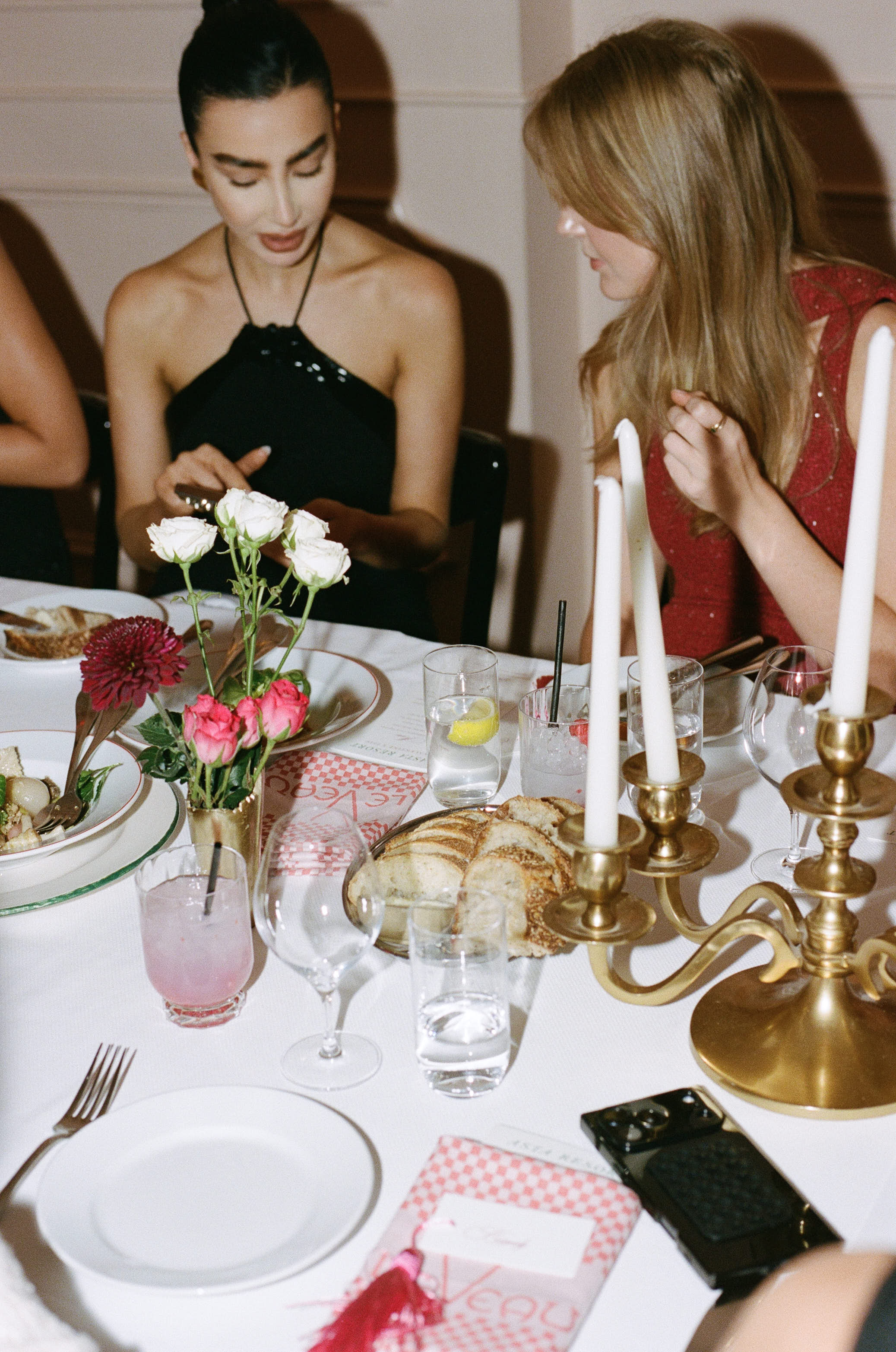 Two women dining at a candlelit table with roses, bread, and pink cocktails